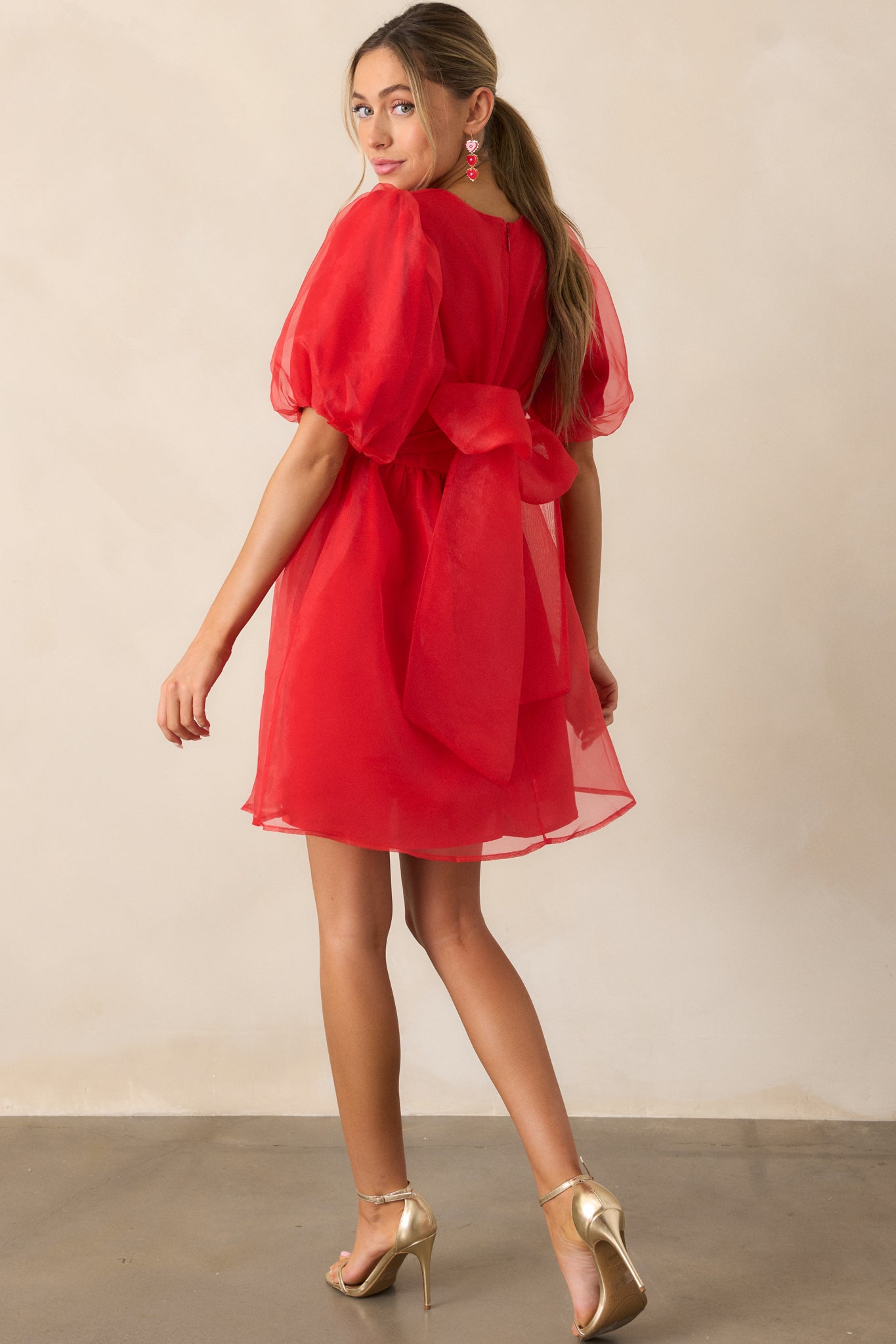 Angled back view of the red mini dress, emphasizing the sheer organza tie and the overall back design.