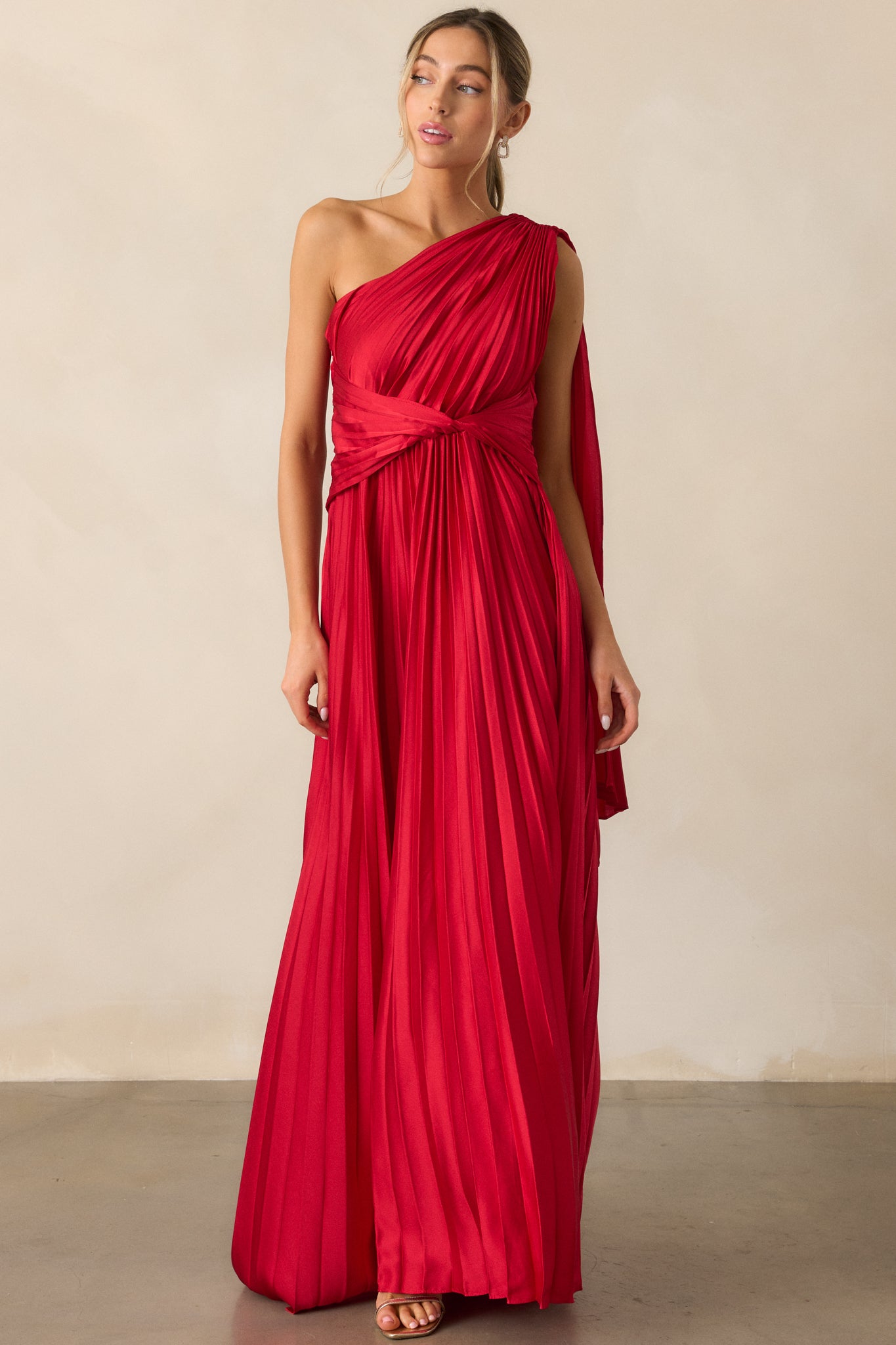 Another chic front view of the dress emphasizing the one-shoulder neckline, twist waist detailing, and the fluid pleated fabric flowing down.