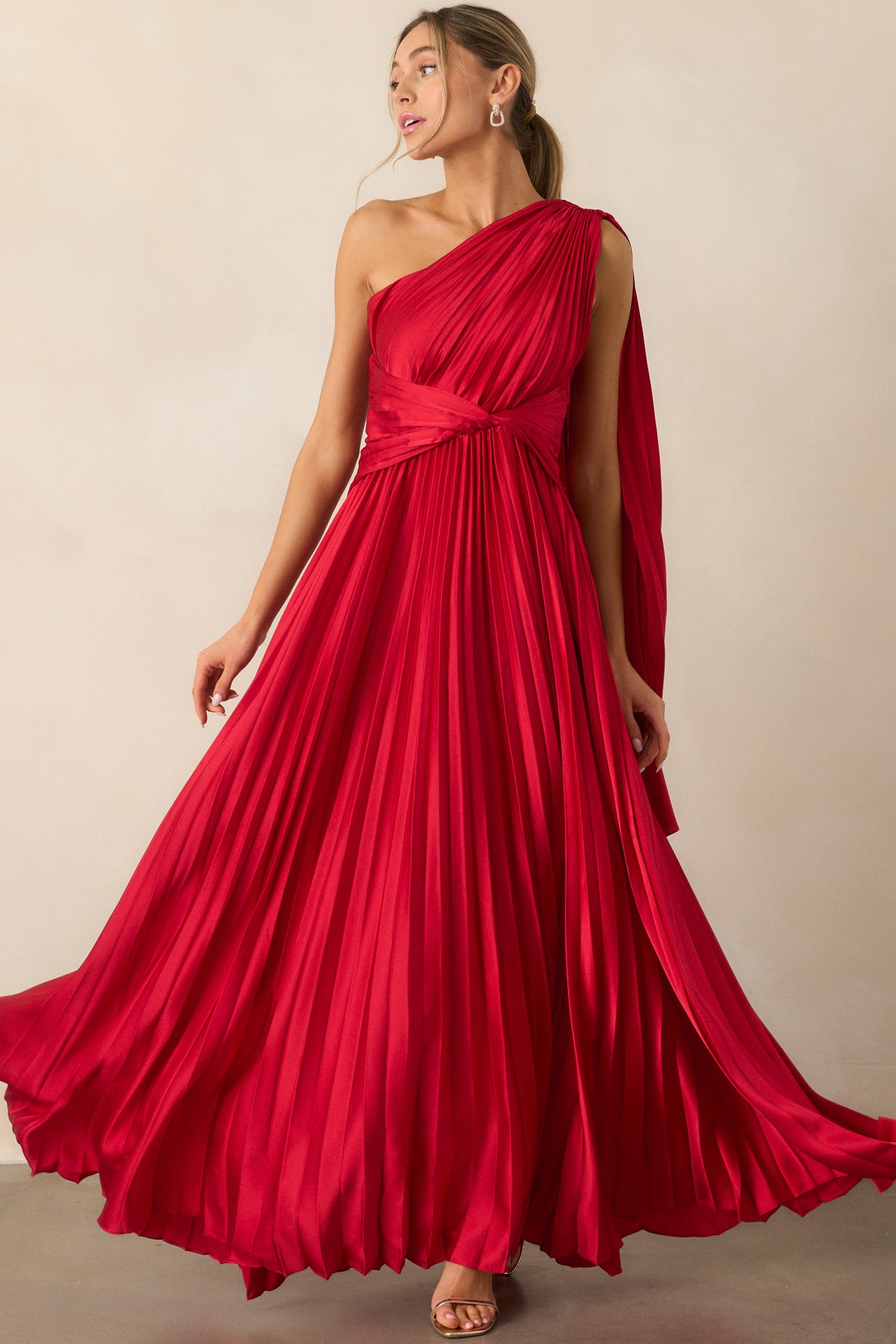 The red dress shown from the front, highlighting its one-shoulder design, pleated fabric, and the elegant twist waist detail.