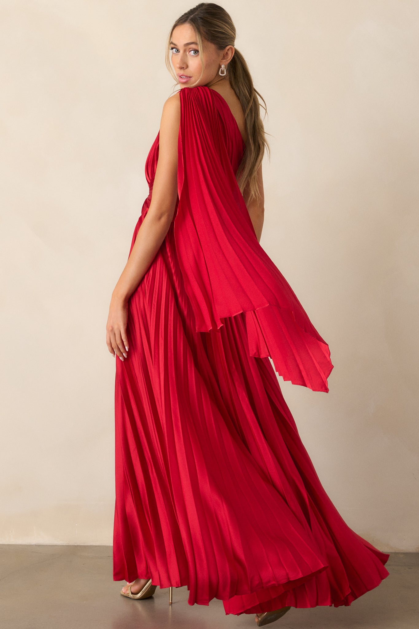 The back of the red dress showing the flowing pleated fabric, highlighting the smooth finish and elegant shoulder scarf detailing.