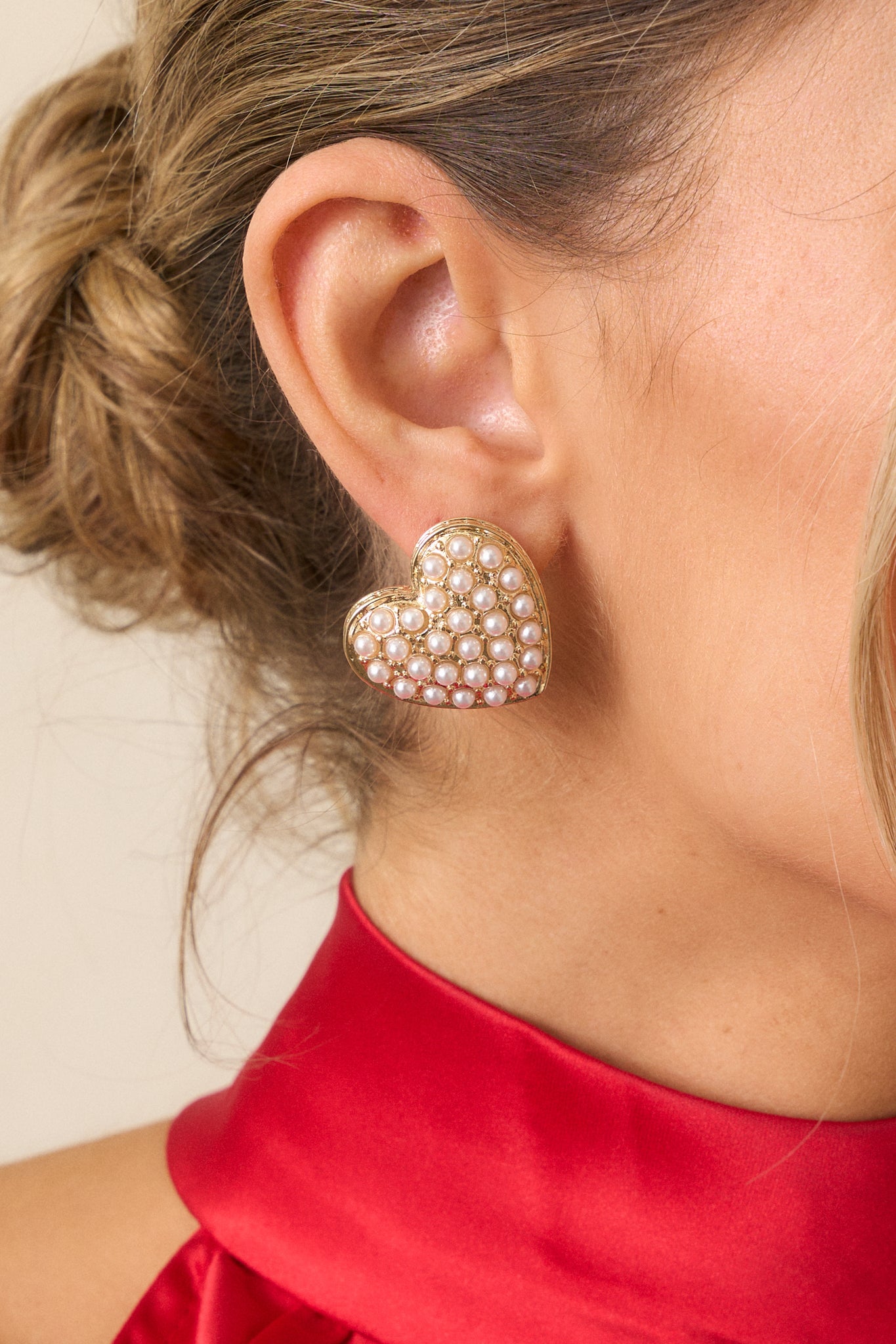 A detailed shot of one earring, emphasizing the intricate arrangement of the small ivory pearls on the heart-shaped gold hardware.