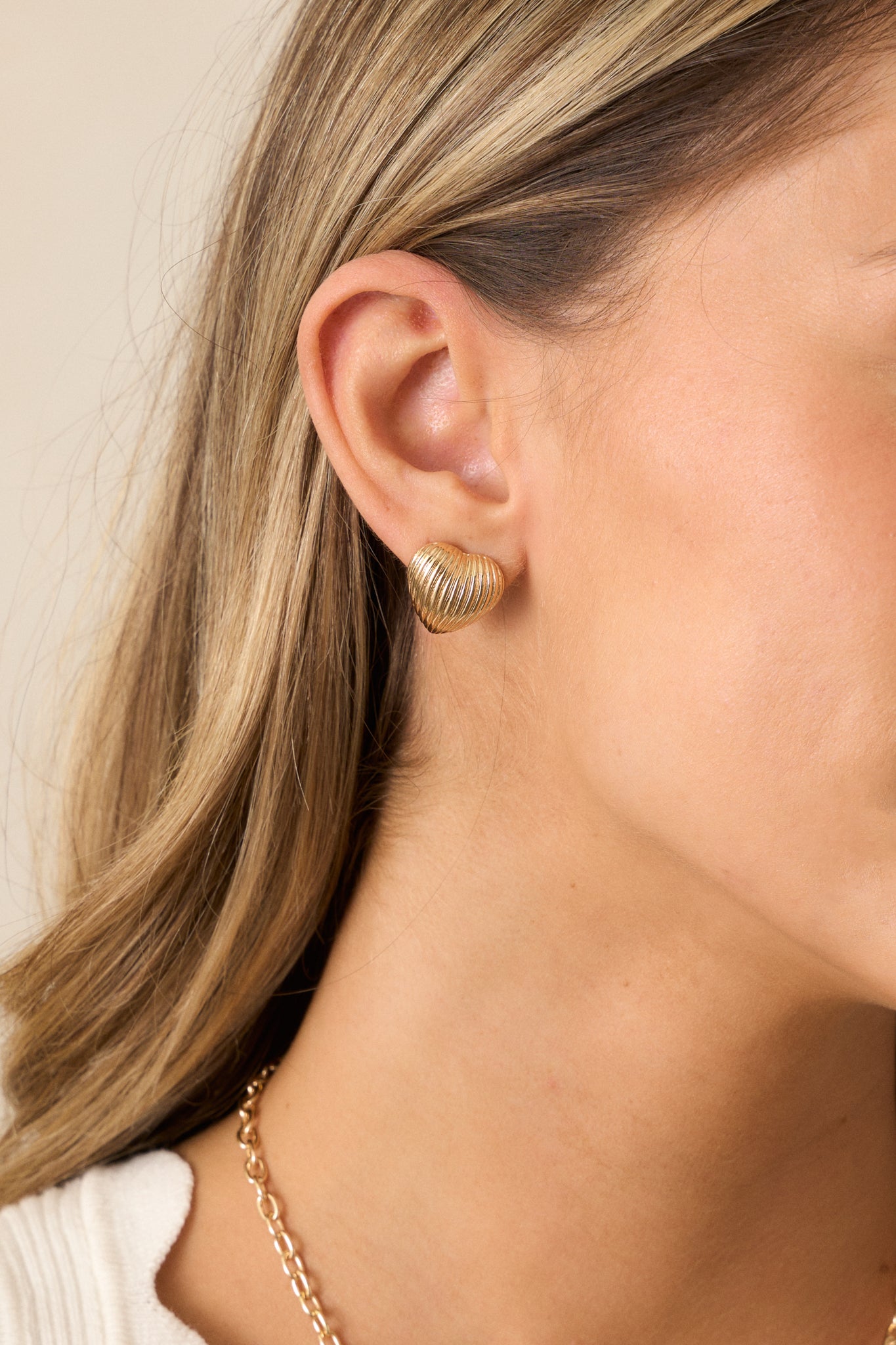 A side angle of a gold heart stud earring highlighting its textured front and sleek gold hardware.