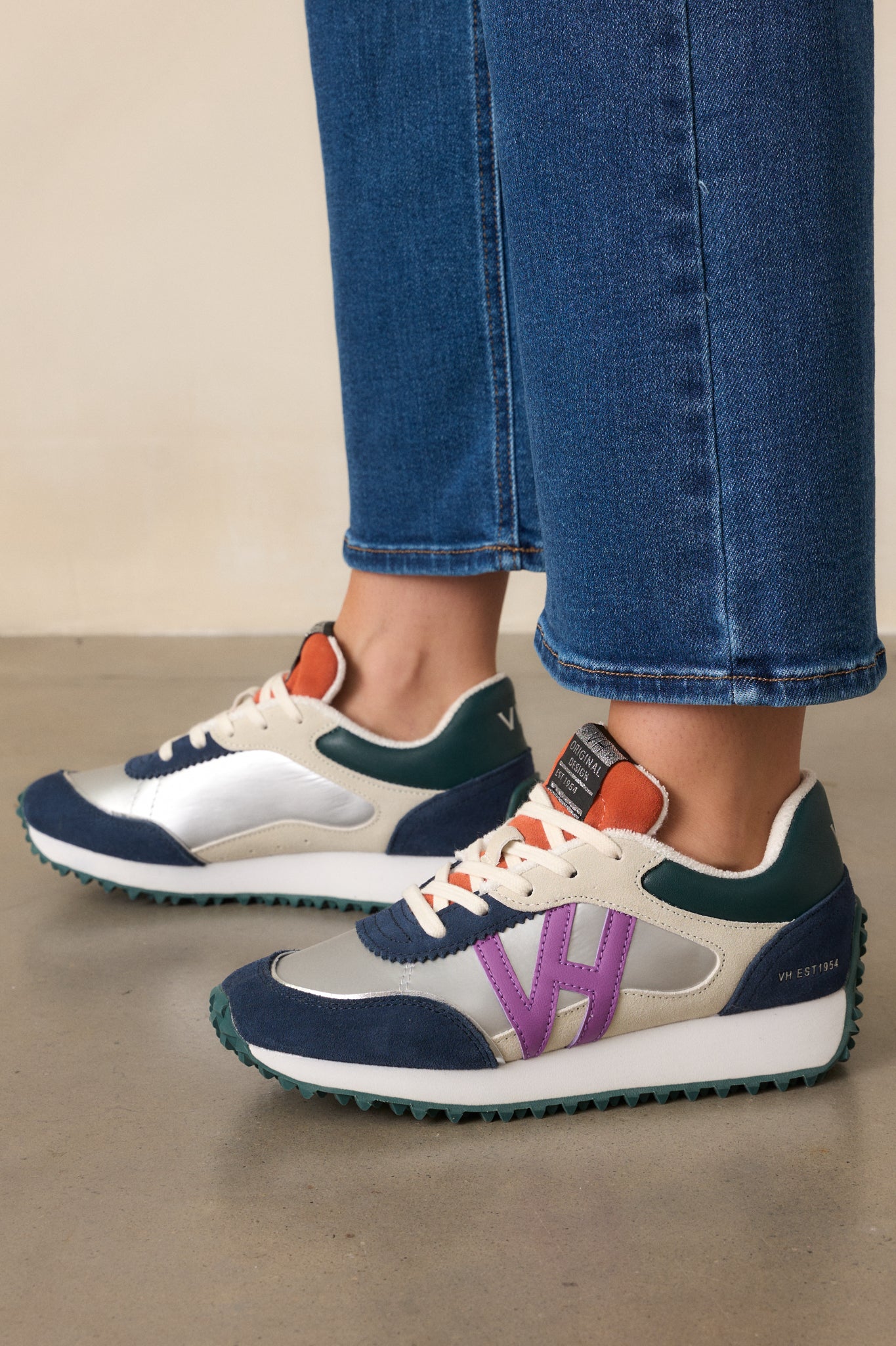 Side image of these silver sneakers that feature a rounded toe, functional laces, subtle pops of purple, navy, orange and silver, a slight platform, and a heavily textured sole.