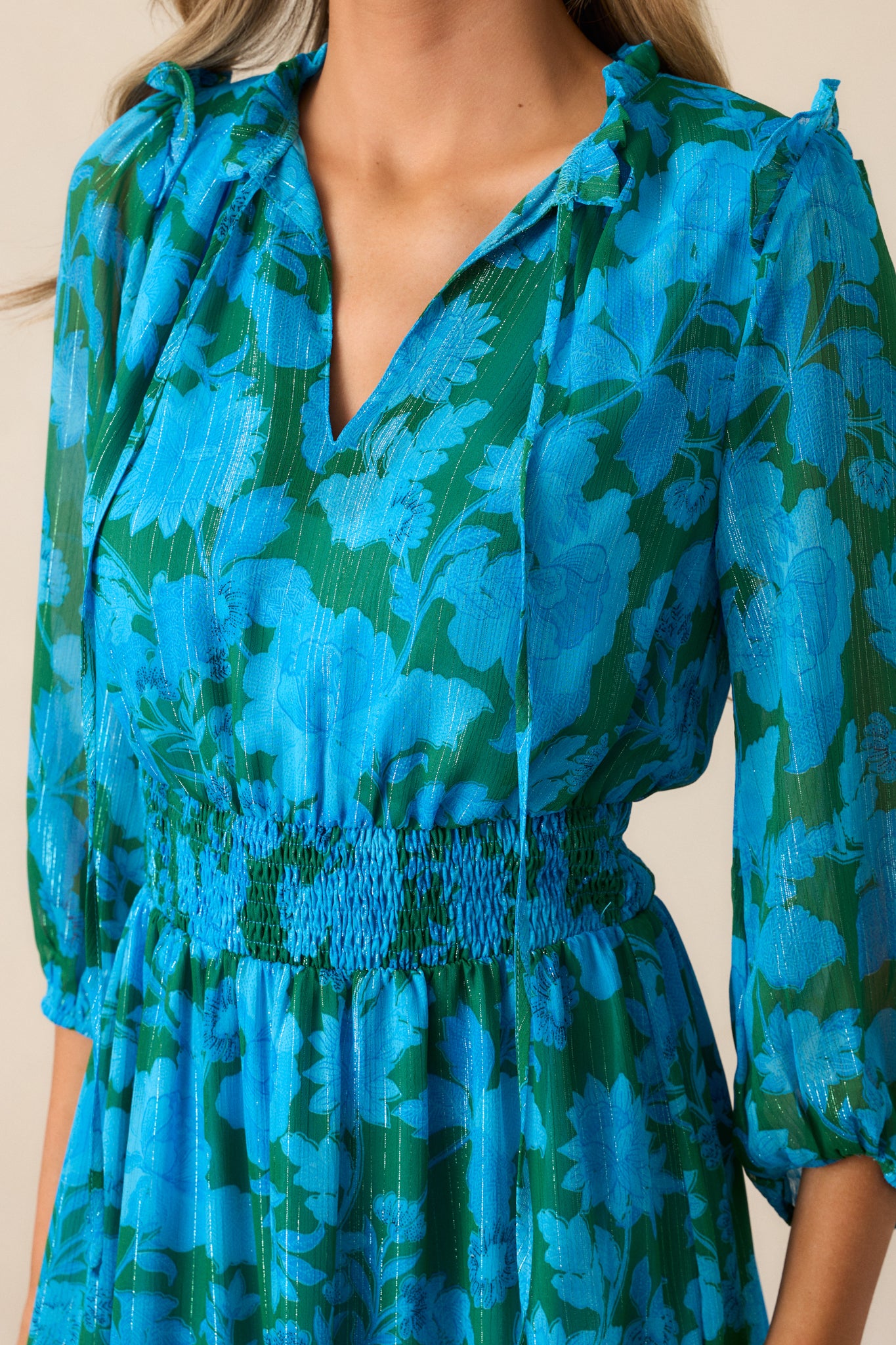 An up-close shot of the v-neckline with self-tie collar detailing and the ruffle shoulder detailing on the blue dress.