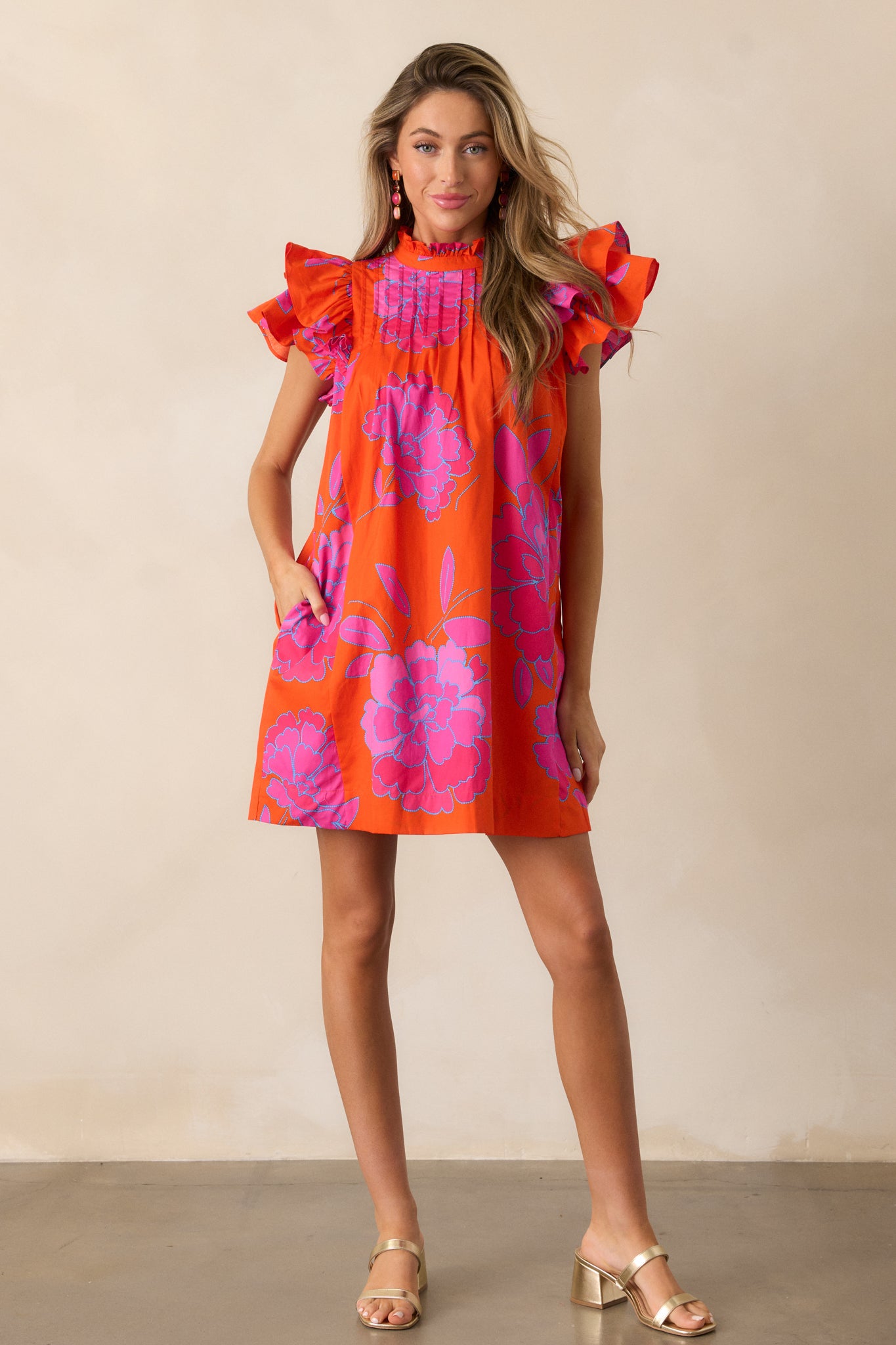 Full view of the orange mini dress with a high ruffled neckline and flutter sleeves, showing the dress's flowing, relaxed silhouette.