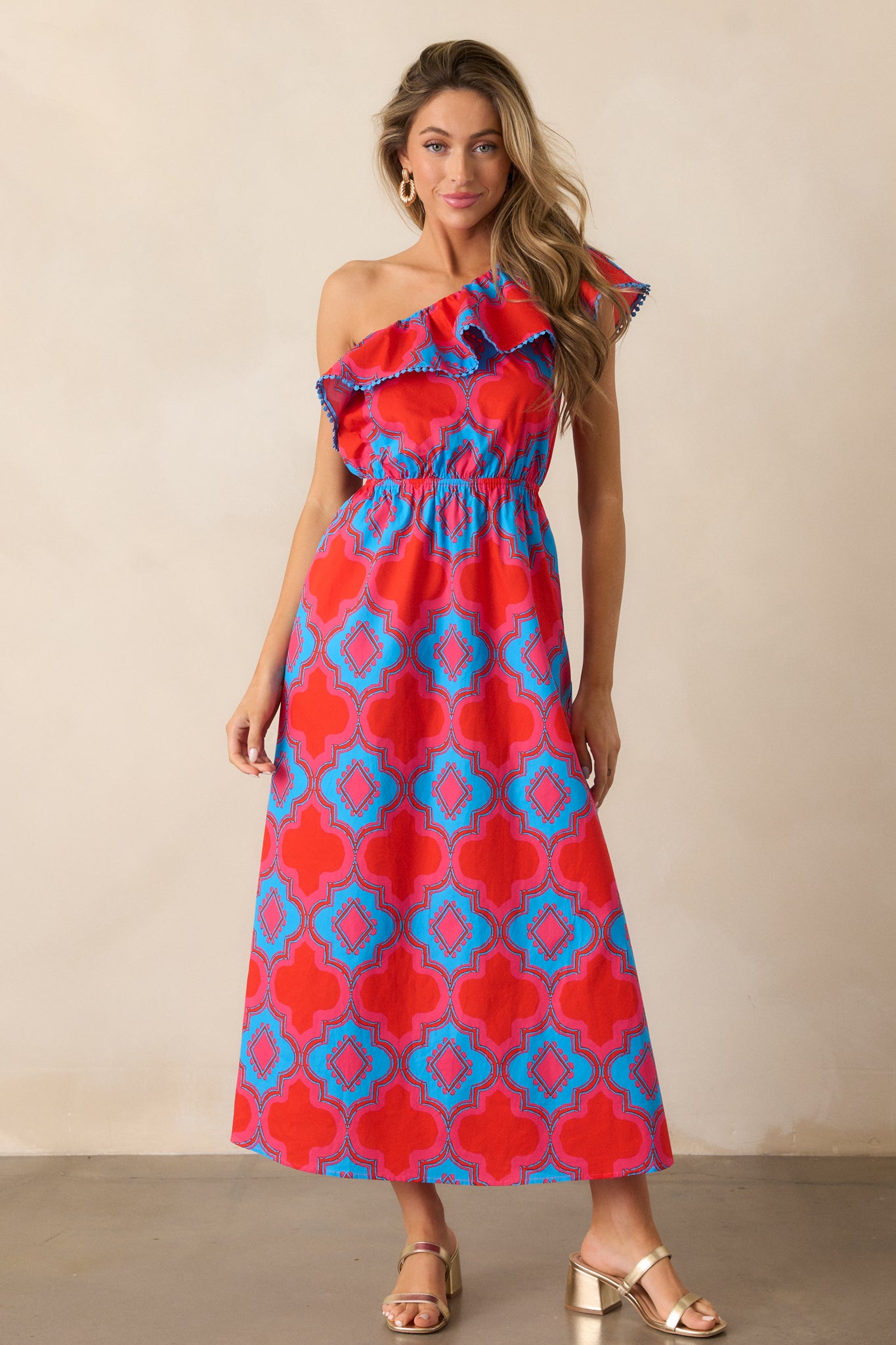  Full-body shot of the red dress, showcasing the one-shoulder silhouette, ruffled neckline, and beautiful blue and pink floral print.