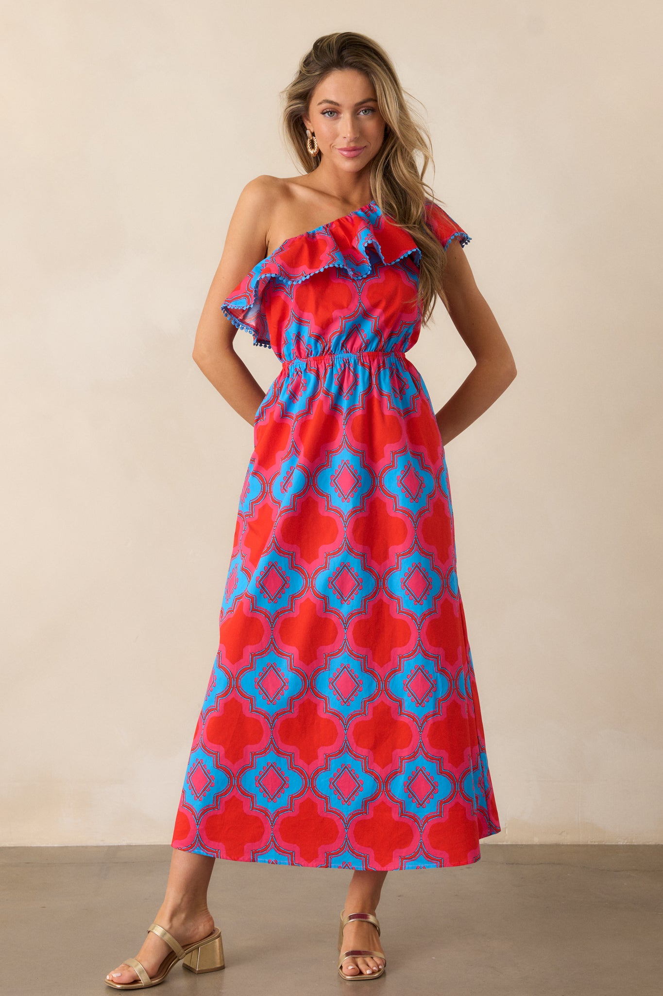 Full-body image of the red dress, emphasizing the elegant one-shoulder design and the lively blue and pink print that covers the entire dress.