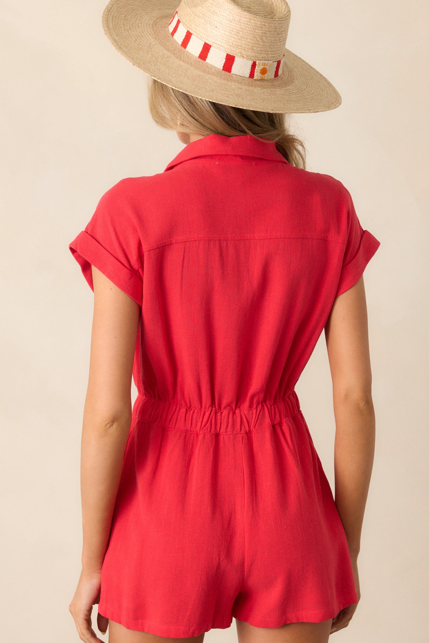 A back view of the red romper, displaying the simple and clean design of the back, along with the elastic waistband and cuffed shorts.