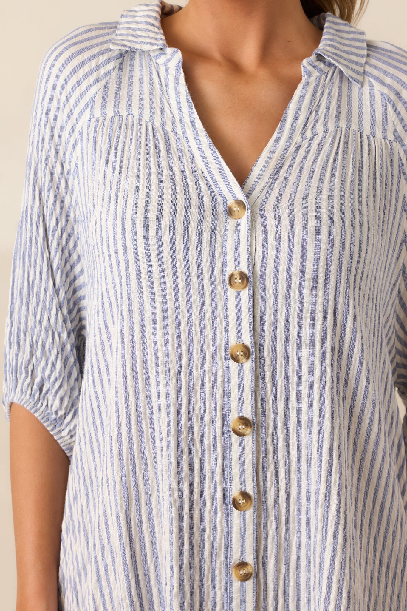 An up-close detail shot of the light blue mini dress’s vertical stripes, button front, and elastic-cuffed sleeve.