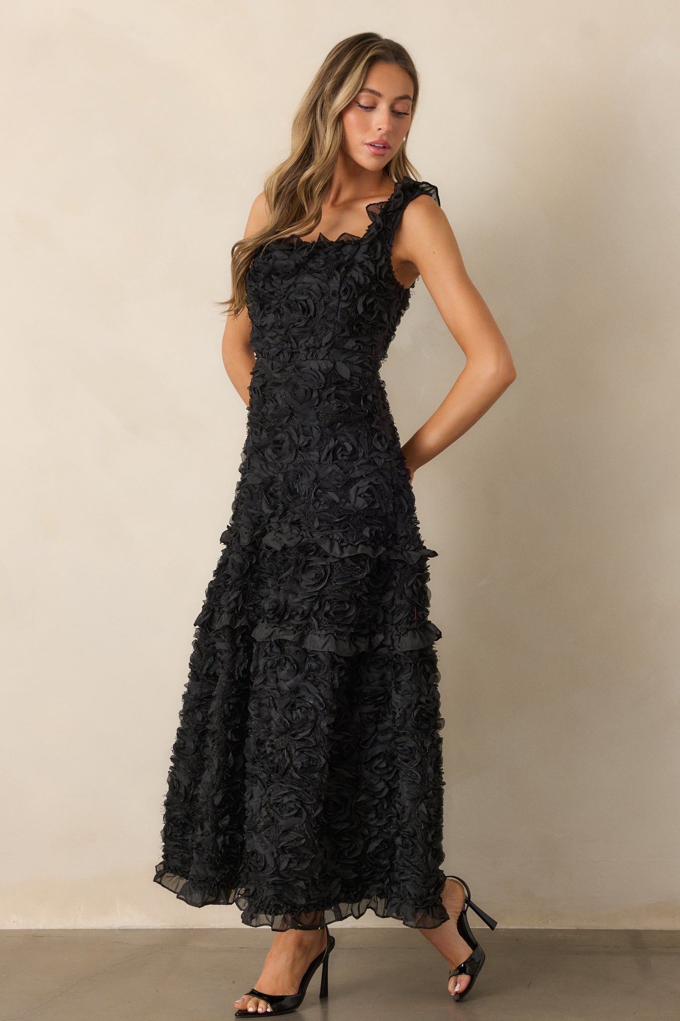 A full-length view of the black dress, showcasing its square neckline, tiered ruffle skirt, and intricate floral applique detailing.