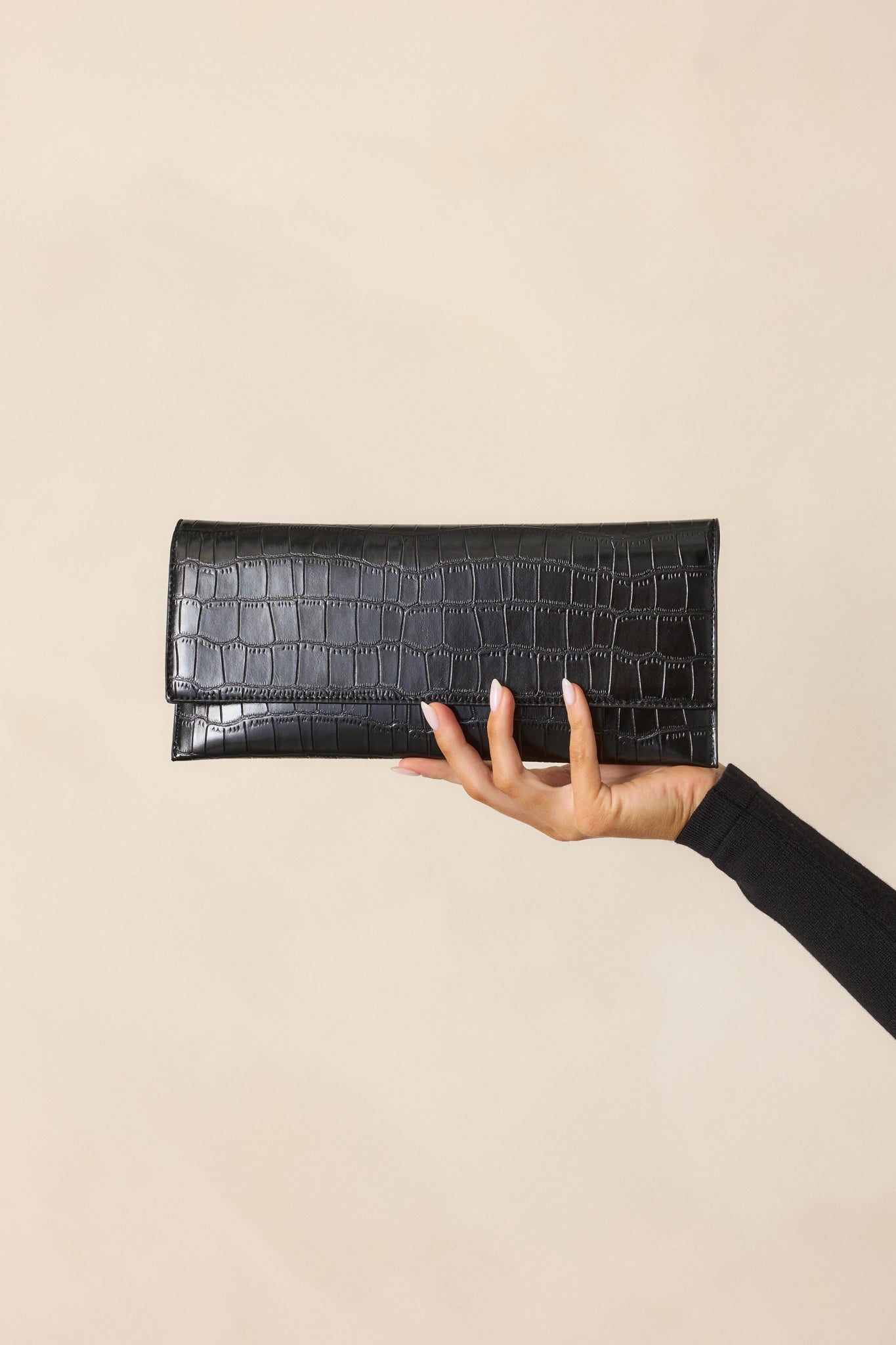 A black clutch with a faux leather textured material, carried in hand, showcasing its rectangular shape and sleek design.