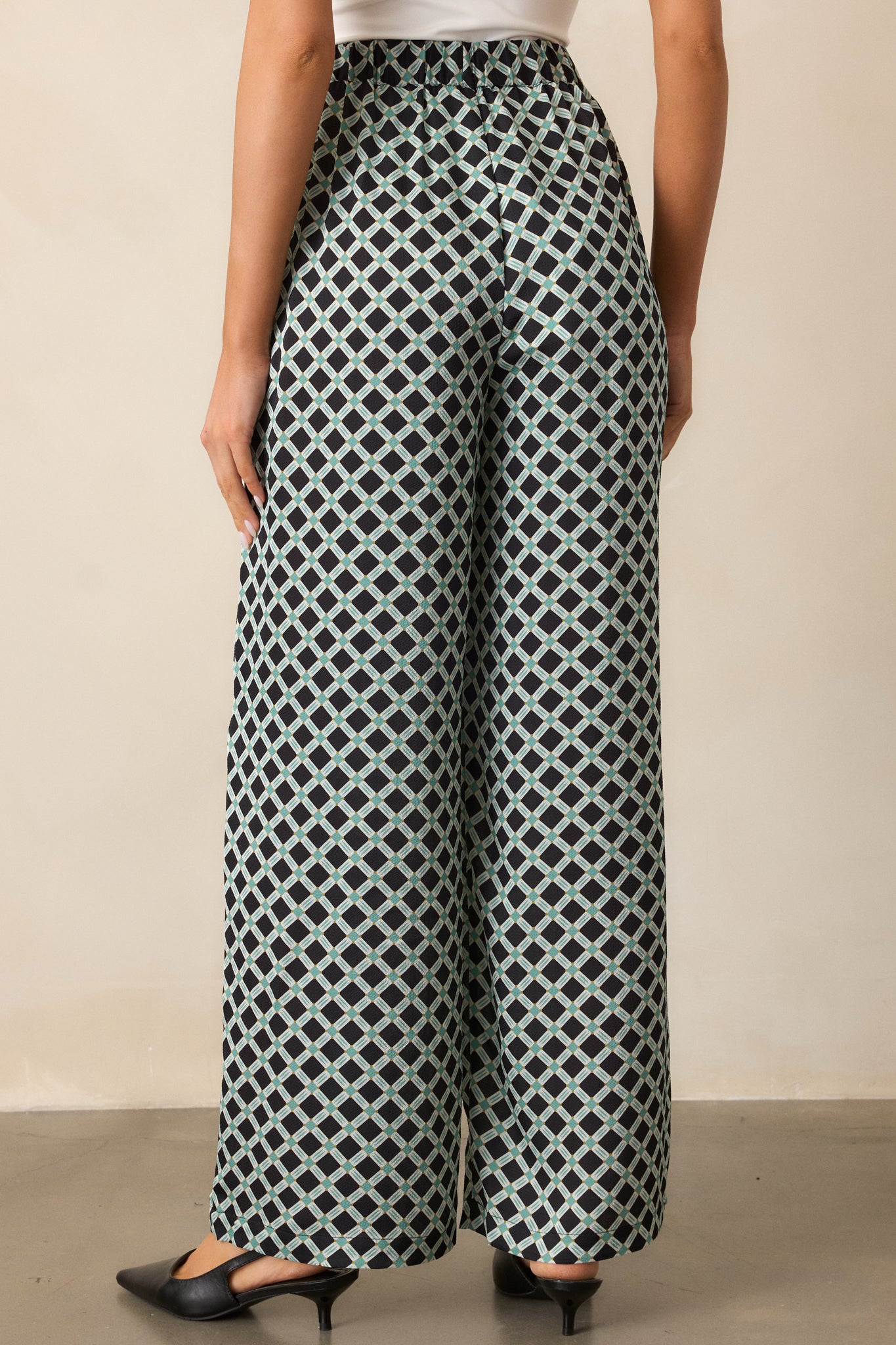 Back view of the black pants highlighting the wide leg cut, high waist design, and continuous green and white geometric print.