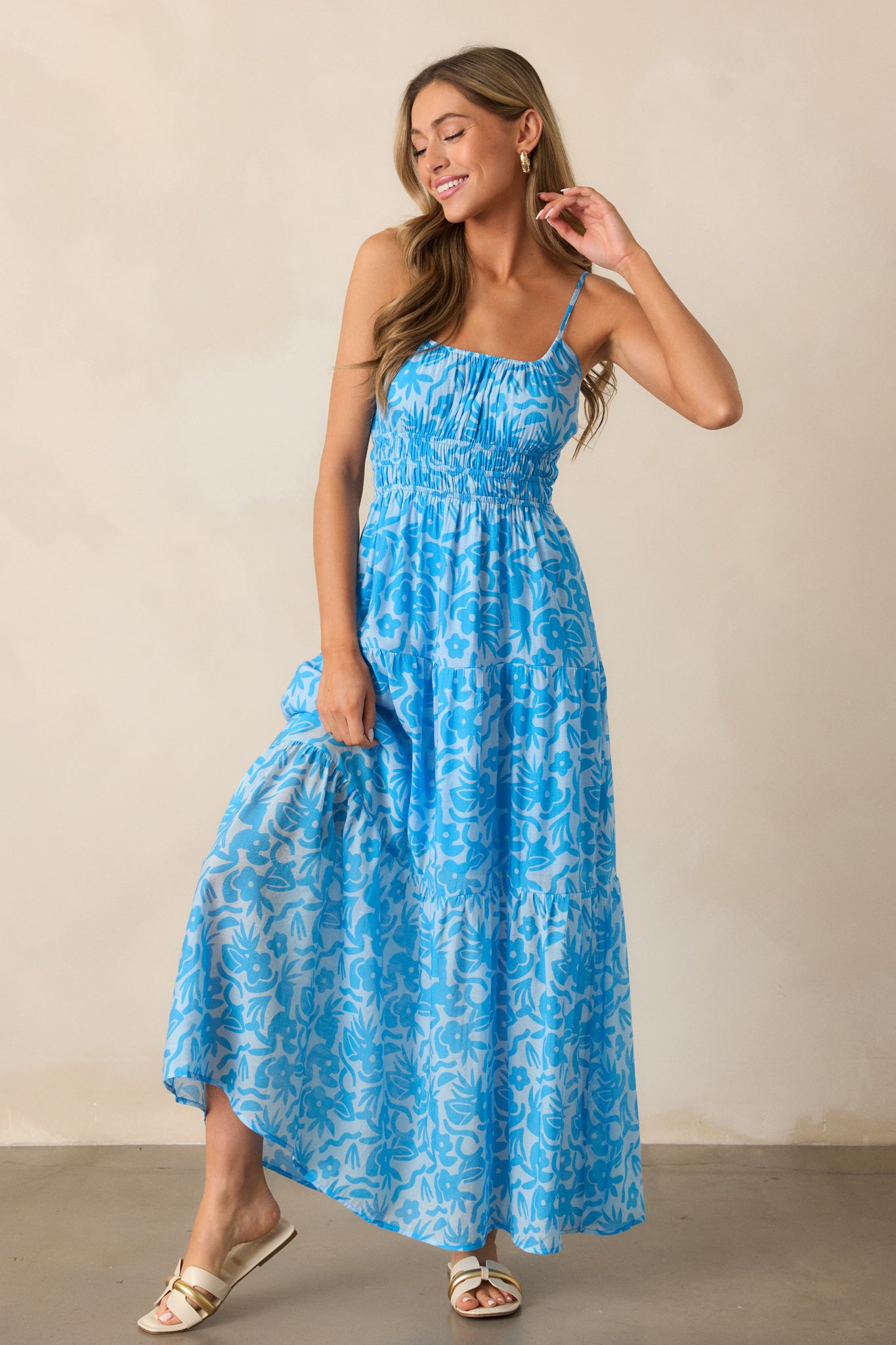  Full view of the blue maxi dress, showcasing the scoop neckline, adjustable spaghetti straps, and the flowing tiered skirt with a vibrant floral print.