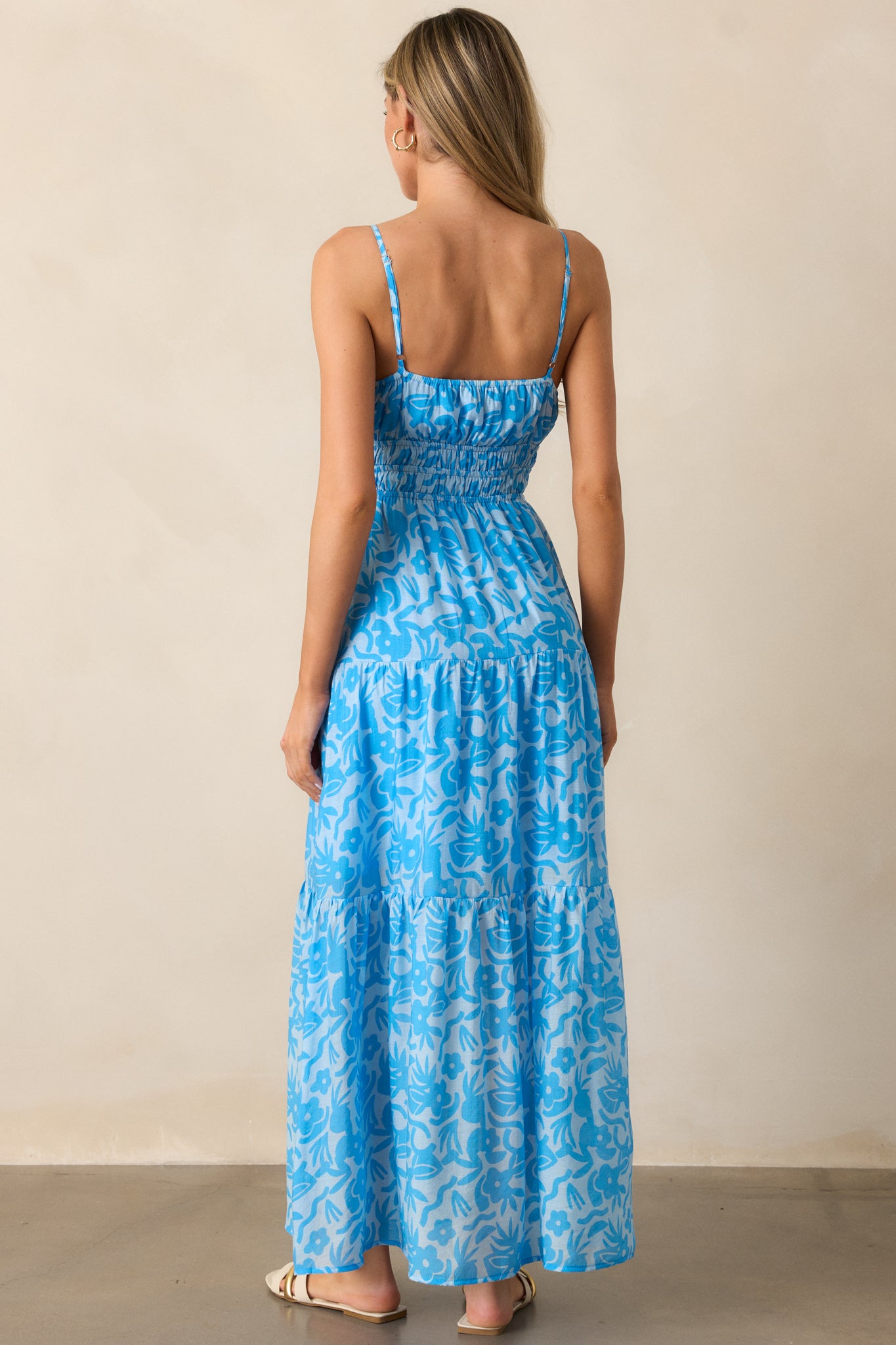 A view of the back of the blue maxi dress, showcasing the adjustable spaghetti straps and the flow of the tiered skirt.