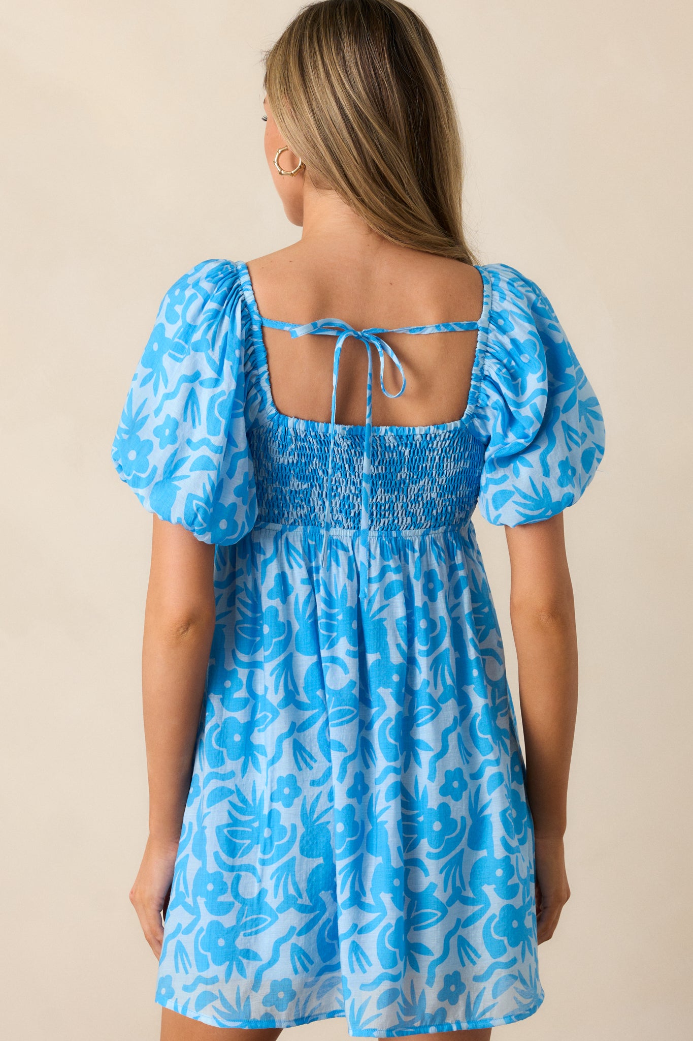 A view of the back of the blue mini dress, highlighting the flowy flared design and the continuation of the floral print.