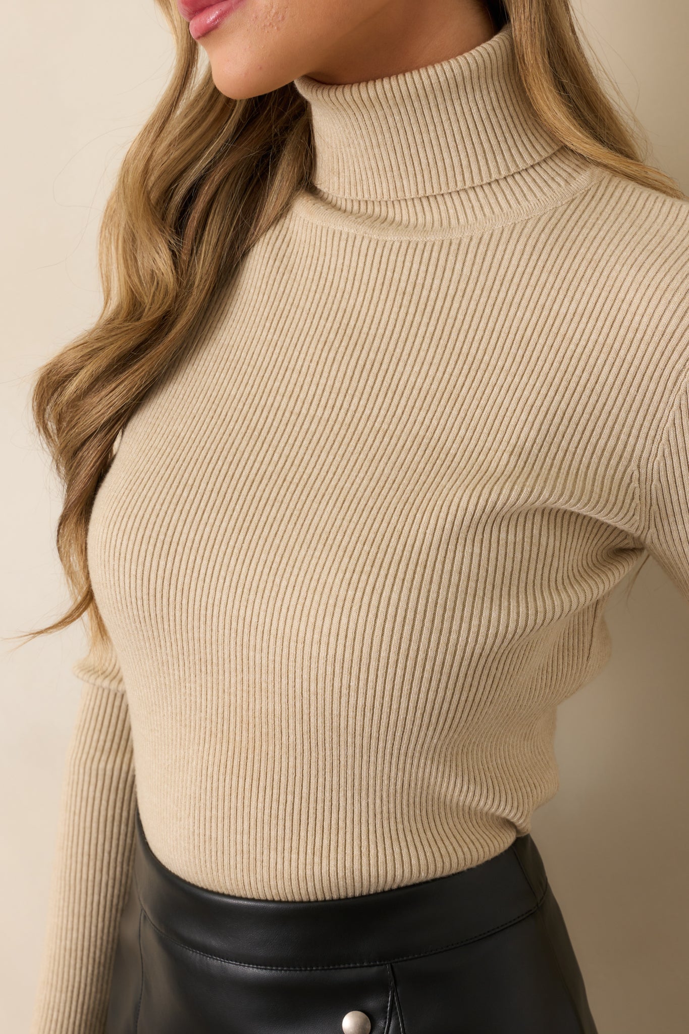 A focused image of the turtleneck and neckline seam, highlighting the ribbed knit design and soft khaki color.