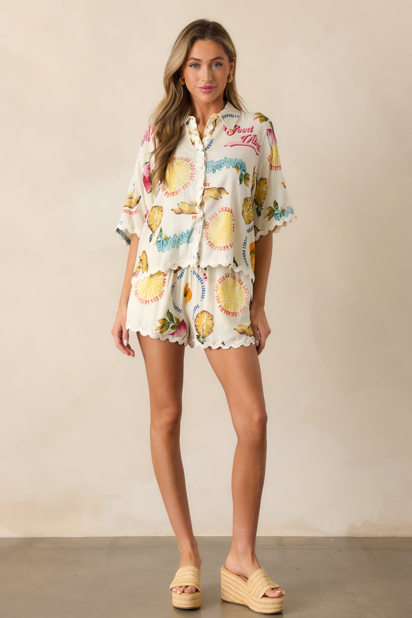 A full view of the ivory top showcasing its collared neckline, colorful tropical fruit print, and oversized short sleeves.