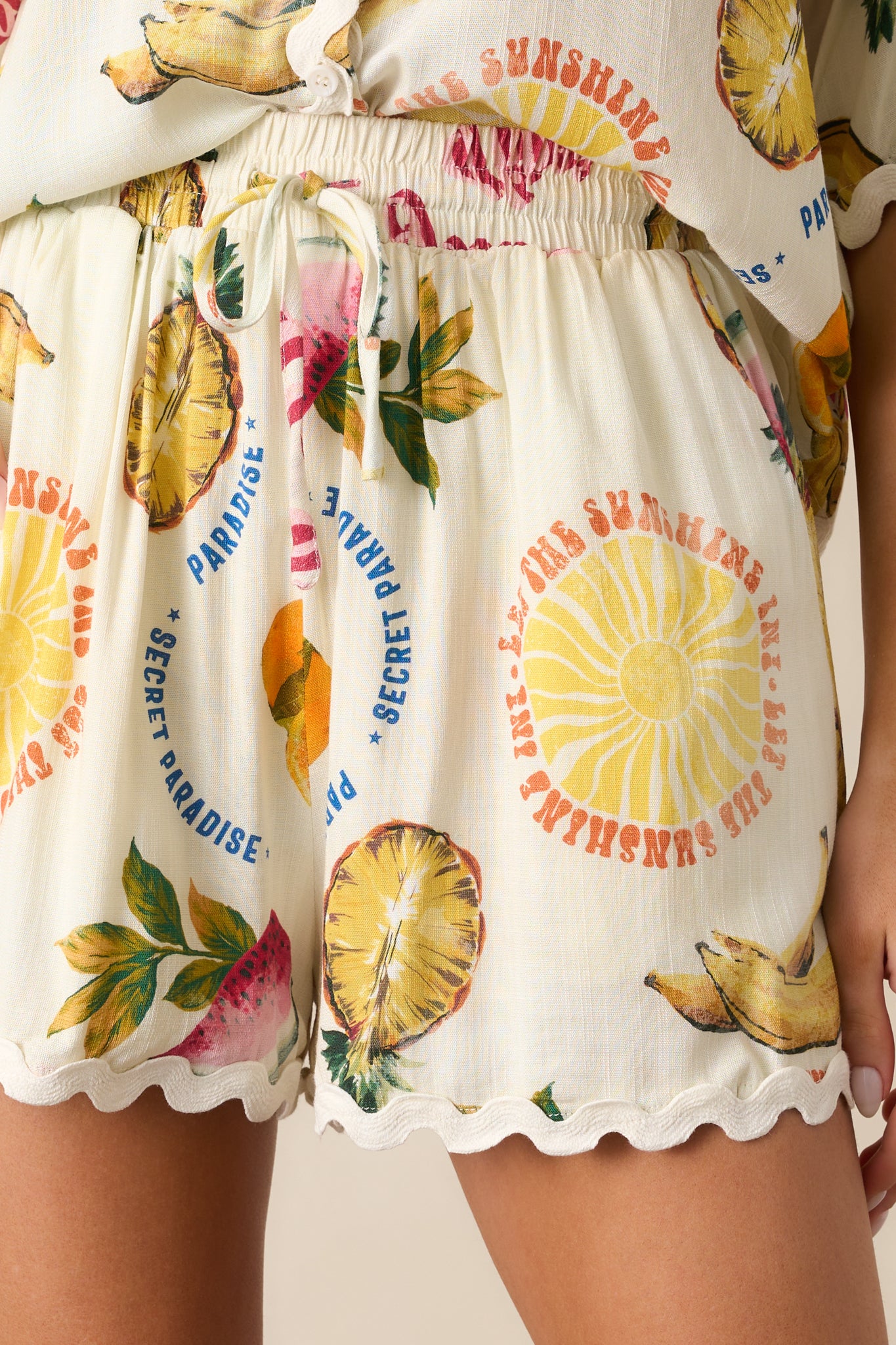 An up-close detail shot of the tropical fruit print and ricrac trim on the ivory shorts.