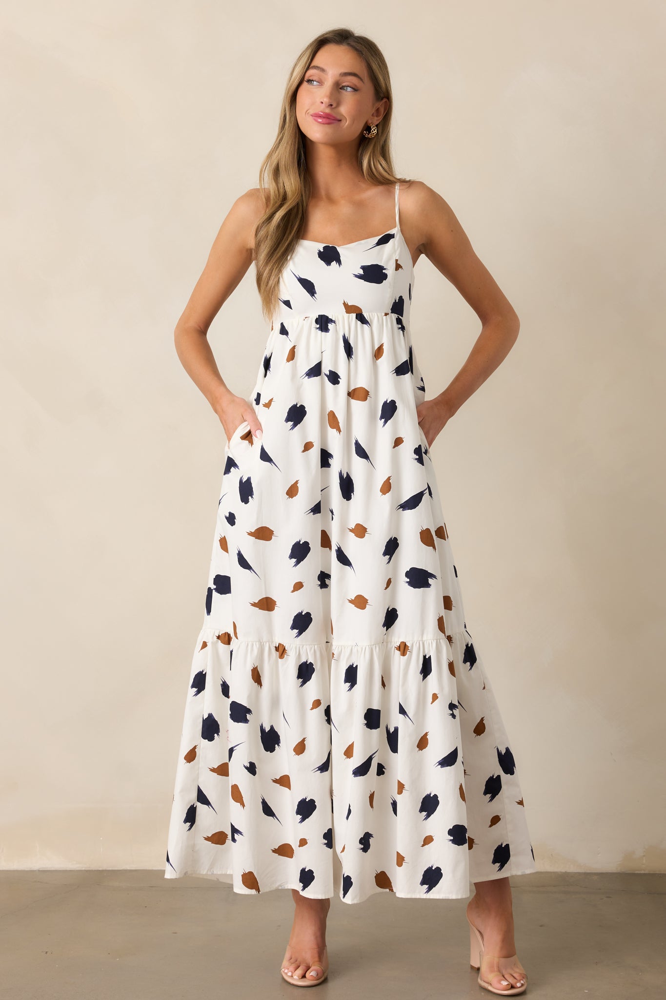 A stylish ivory maxi dress showcasing a bold brown and navy brush stroke print, straight neckline, and adjustable straps for a customizable fit.