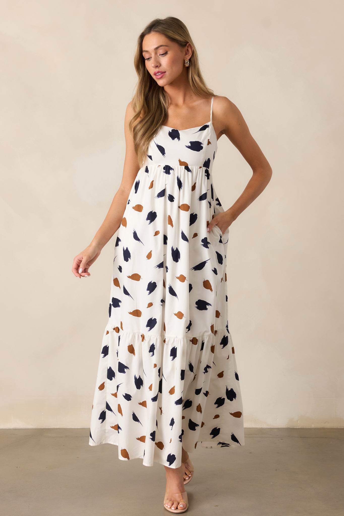 Maxi-length ivory dress with a straight neckline, adjustable spaghetti straps, and an artistic brown and navy brush stroke print.