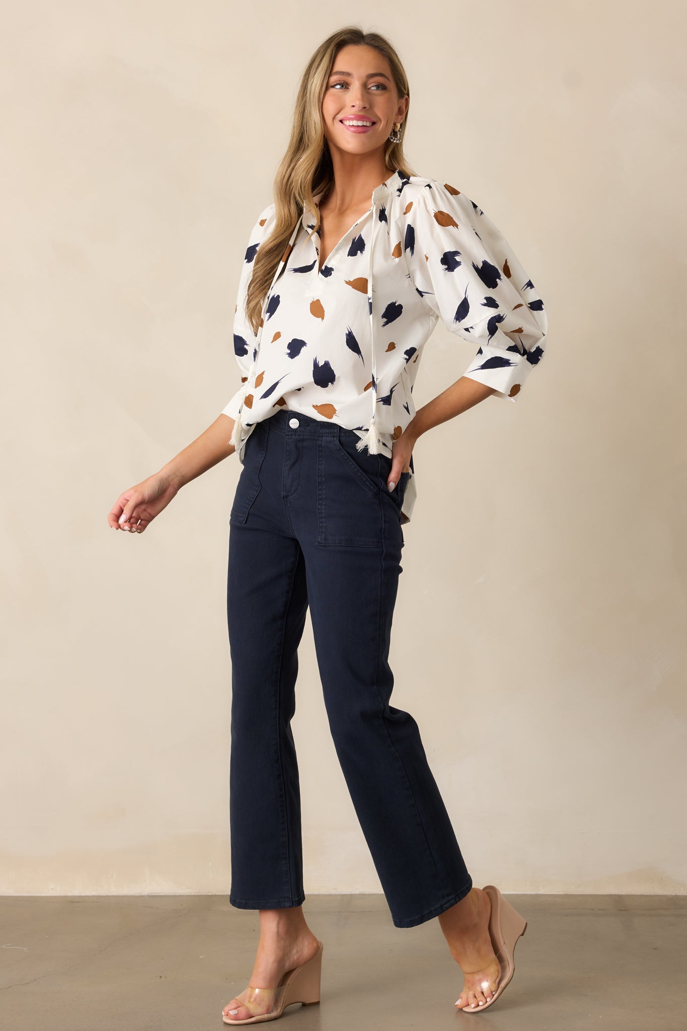 Ivory blouse with 3/4 sleeves, cuff detailing, a v-neckline, and a flowing design highlighted by a brush stroke pattern in brown and navy.