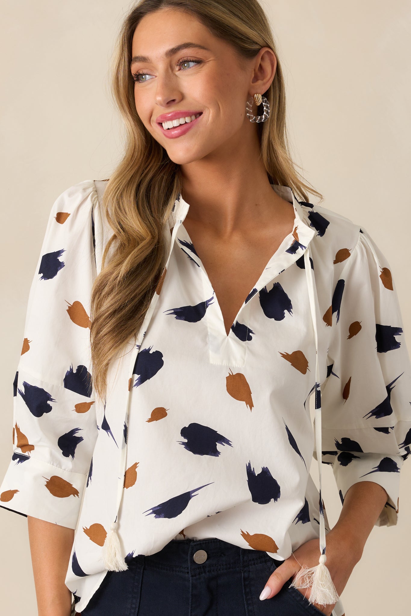 A focused view of the ivory blouse’s v-neckline with a self-tie collar and bold brush stroke print.