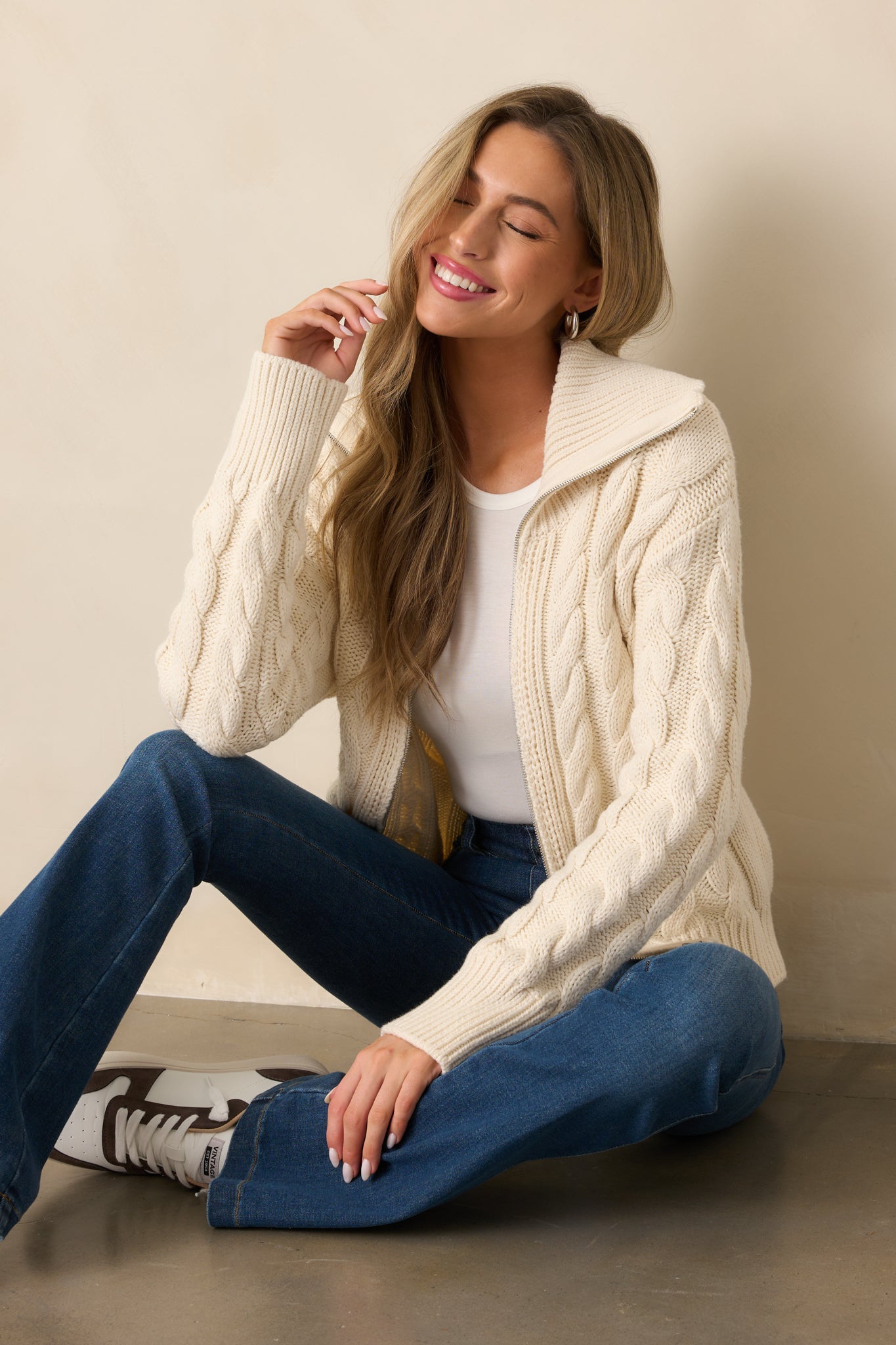 A versatile ivory seasalt cardigan with a silver front zipper, cable knit design, and ribbed cuffs, blending comfort with timeless detail.