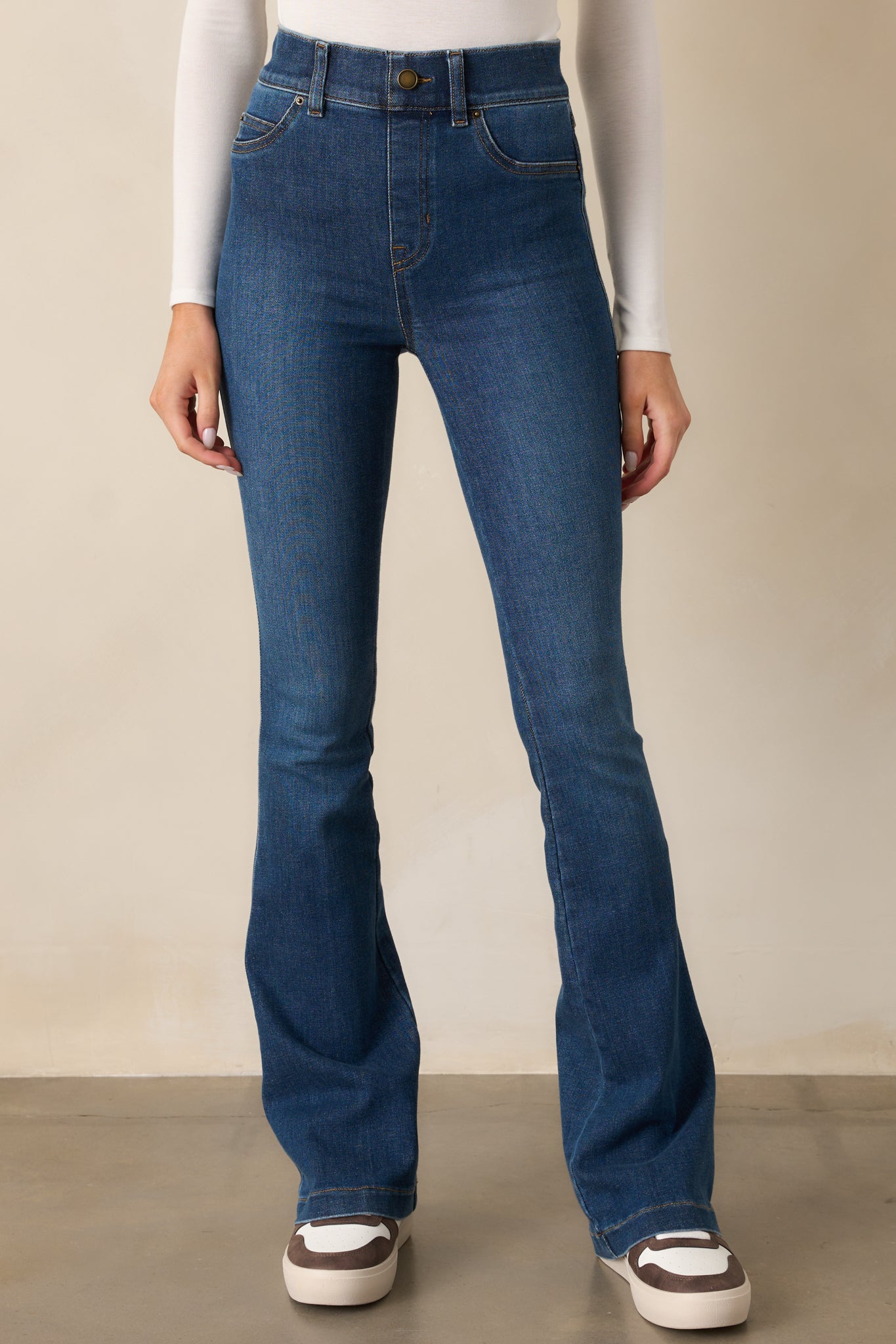 A close view of the high-rise waistband and faux buttons on the blue jeans, highlighting their streamlined pull-on design.