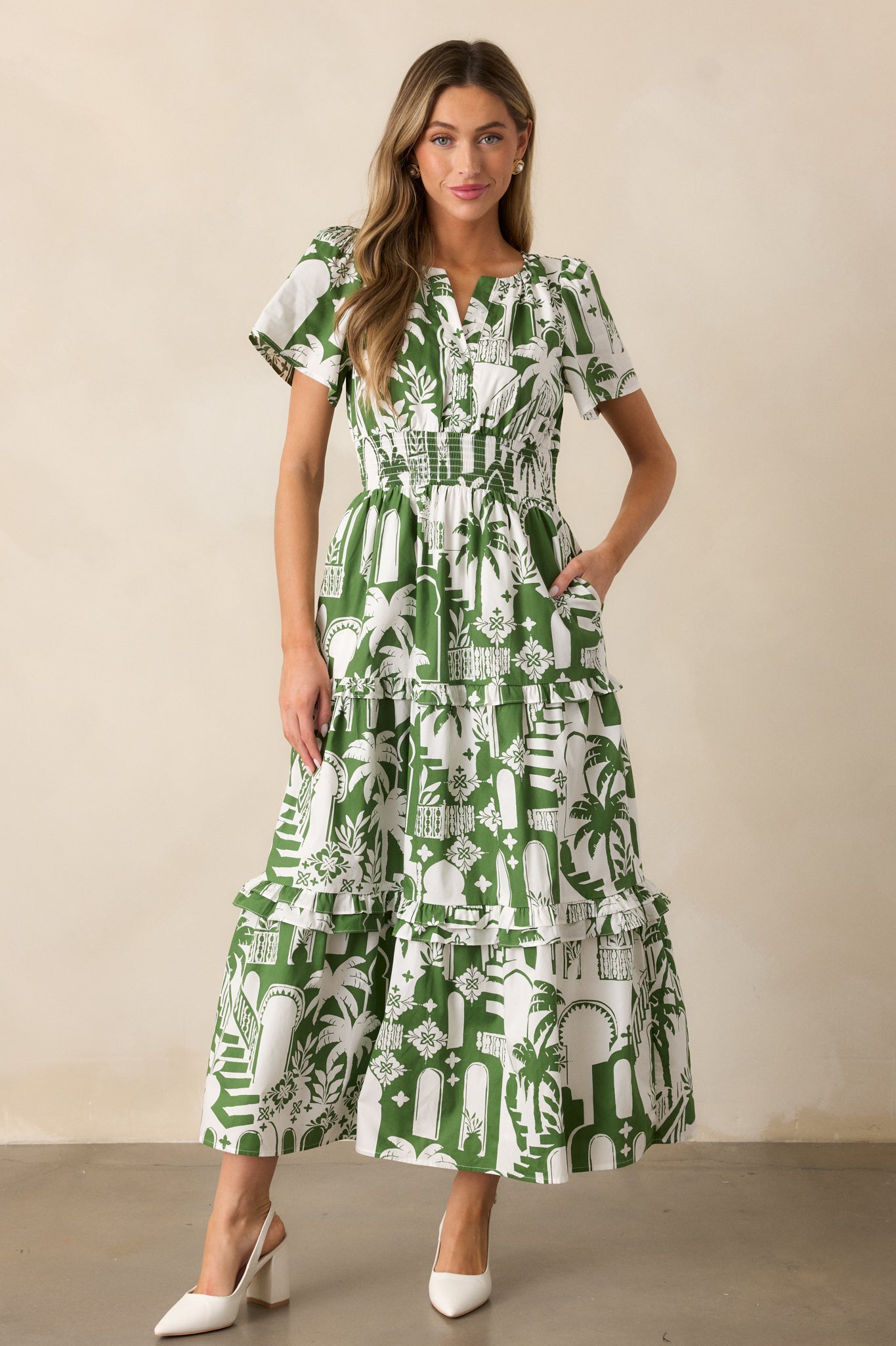 A full view of the green dress featuring a notch neckline, smocked waistband, and short sleeves, with a relaxed tiered skirt and tropical palm print.