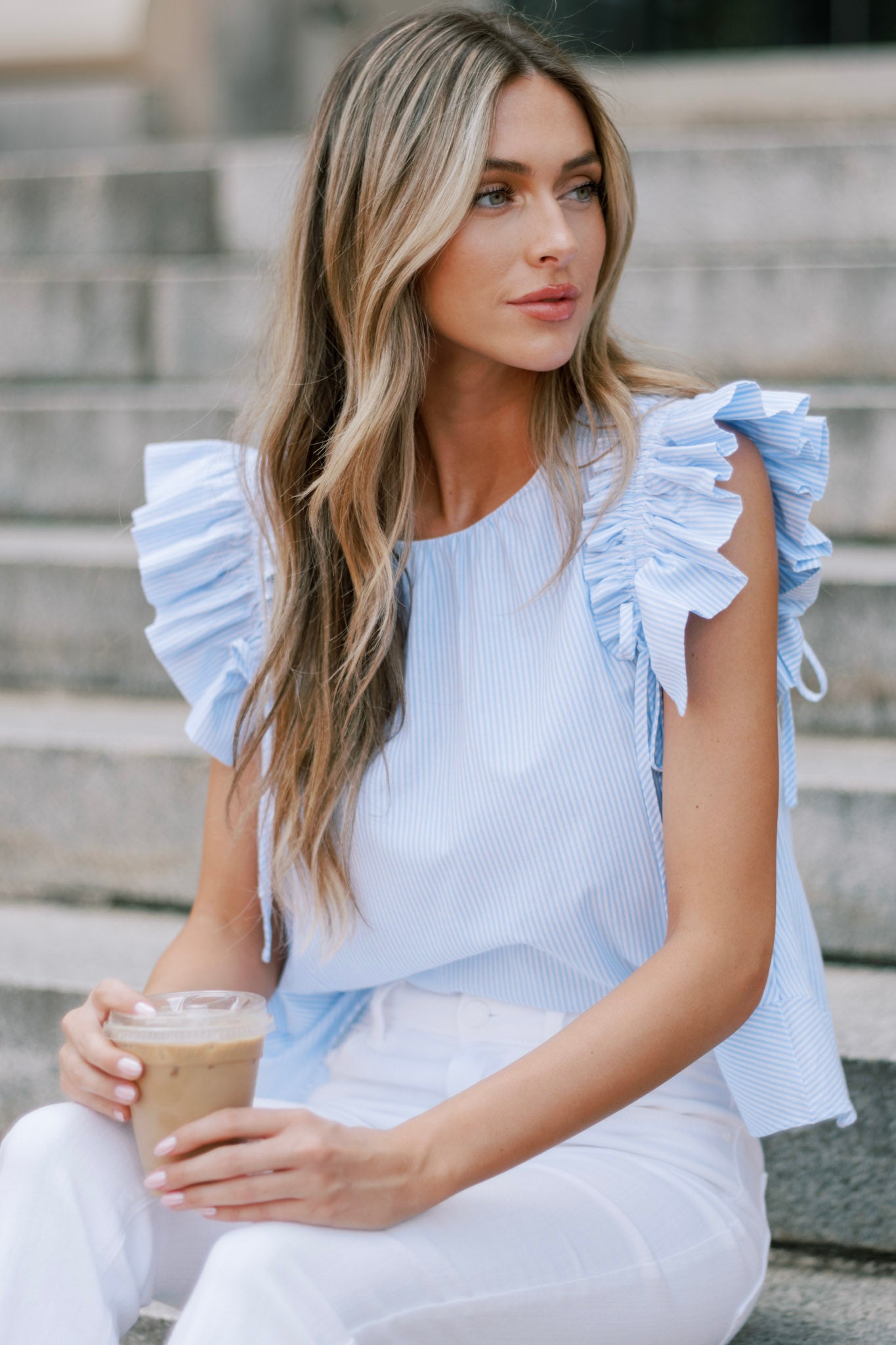 This blue stripe top features a relaxed fit, a crew neckline, vertical stripes, and layered ruffle sleeves with adjustable bows for a custom fit.