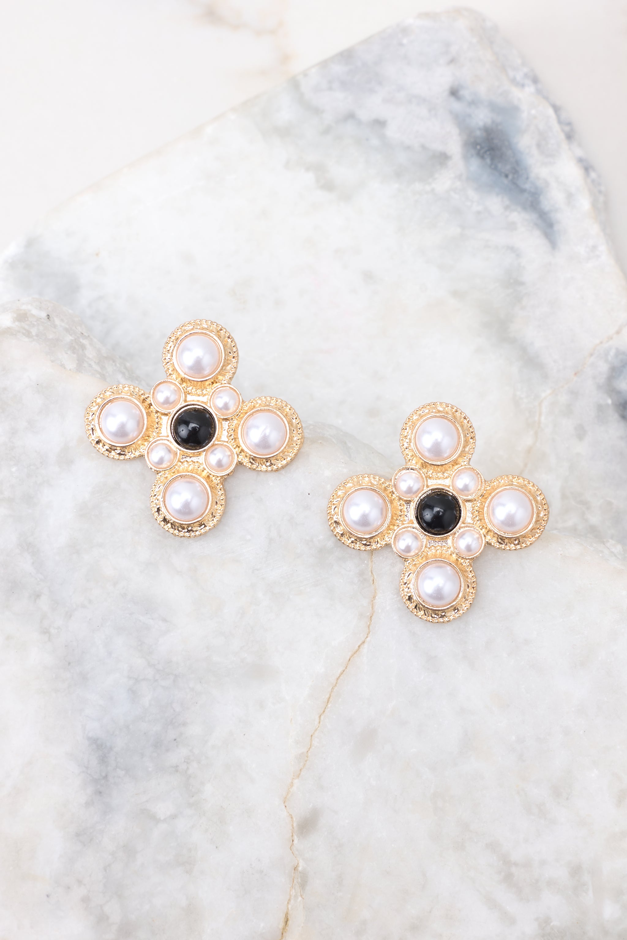 Close-up of these earrings that feature a fun abstract shape, gold hardware, and white and black pearl detailing.