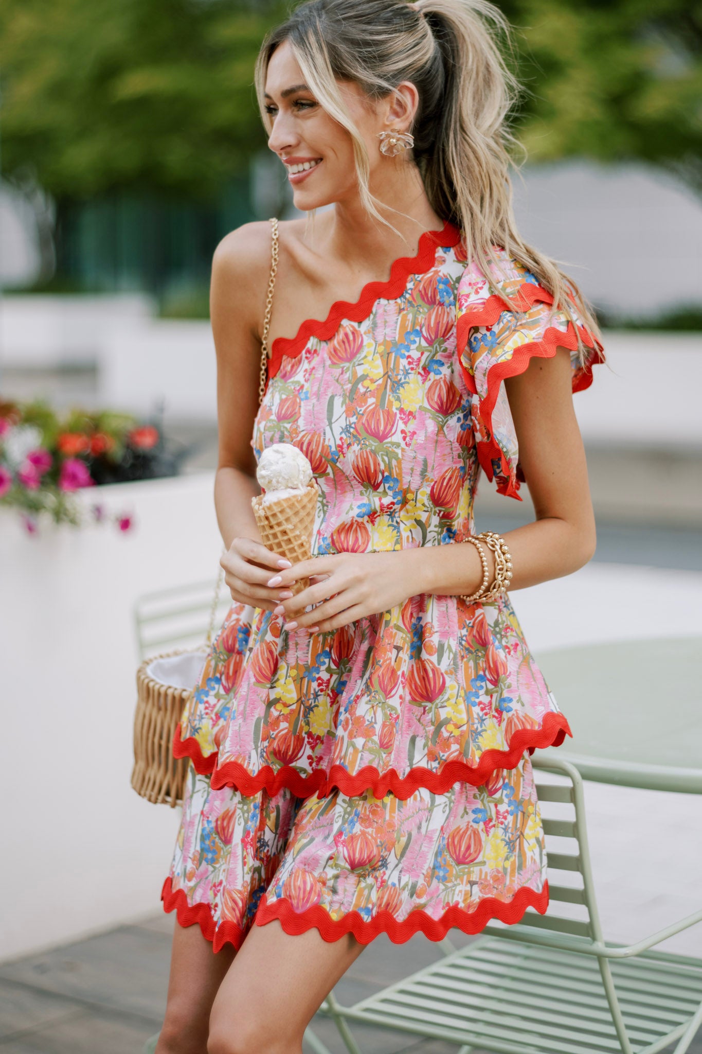 Focused view on the ricrac detailing and floral print of the red multi floral romper, along with the one shoulder neckline.