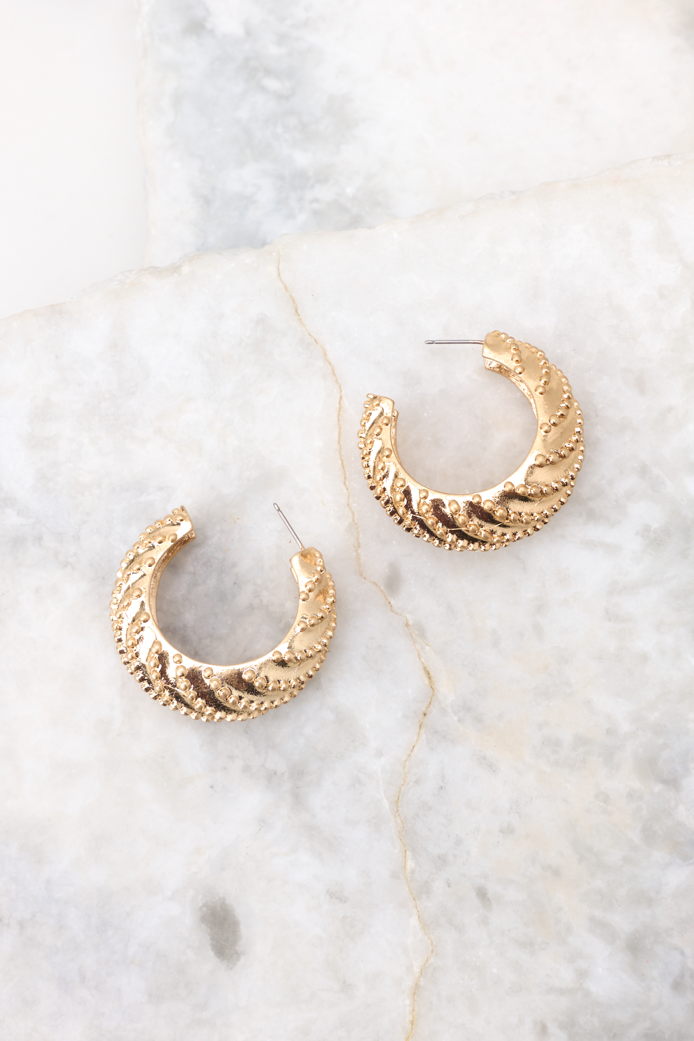 Overhead marble shot of earrings that feature gold hardware, a studded texture, and a secure post backing