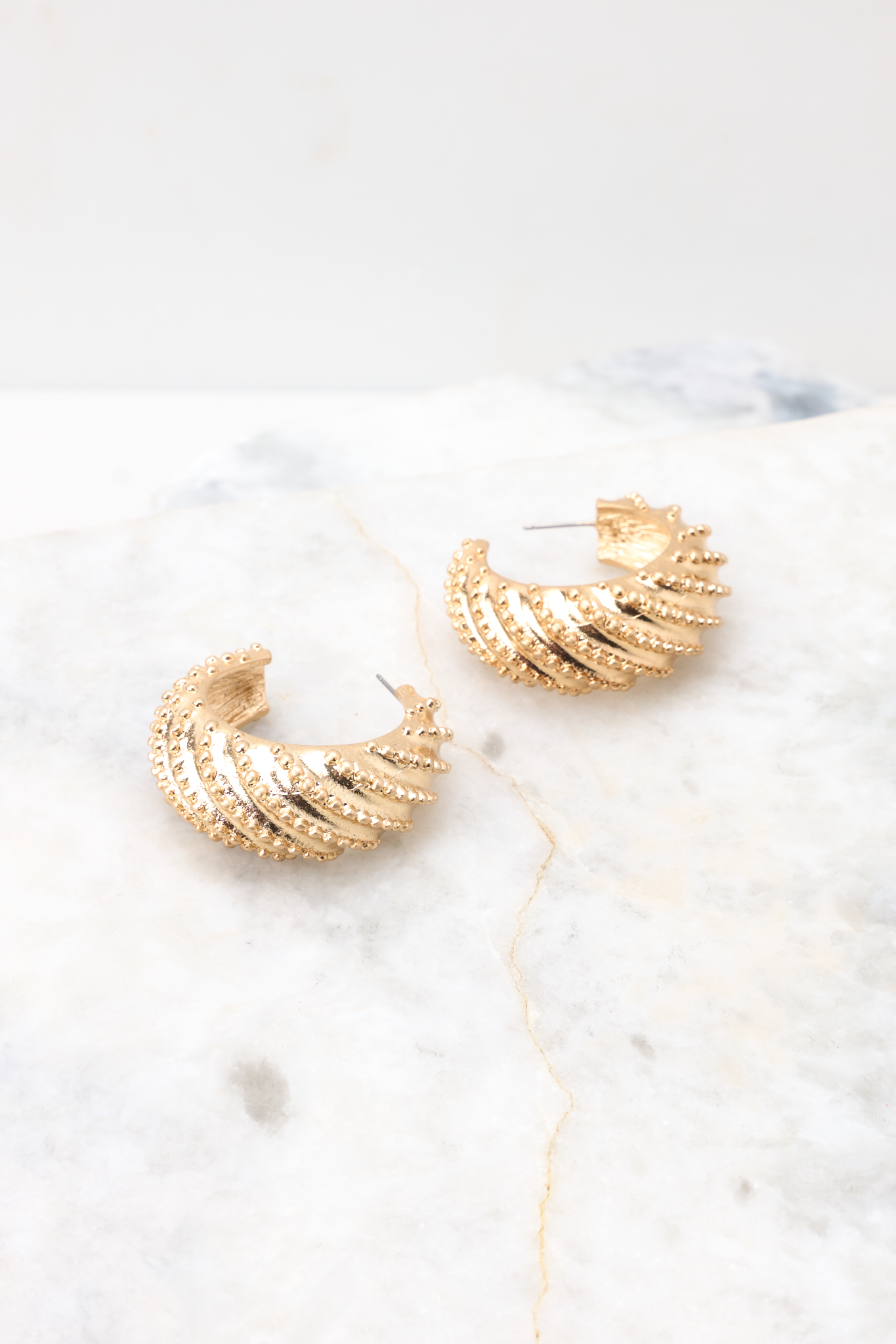 Detailed side view of earrings that feature gold hardware, a studded texture, and a secure post backing