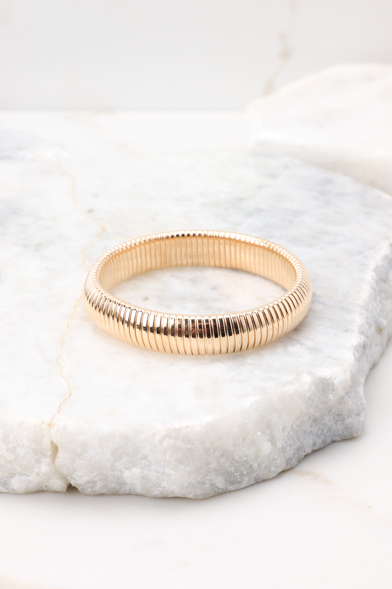 Detailed view of gold bracelet that features a circular, slip-on design with ridge detailing.