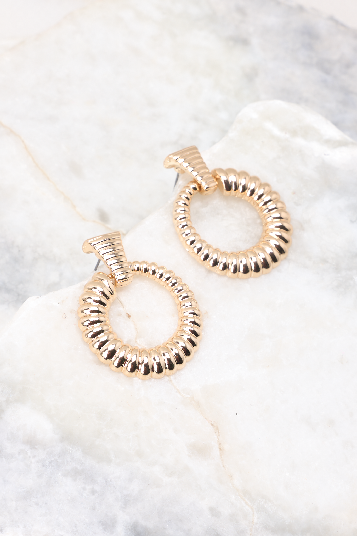 Close up view of these ribbed stud earrings attached to a ribbed hoop. Ribs increase in size around the hoop.