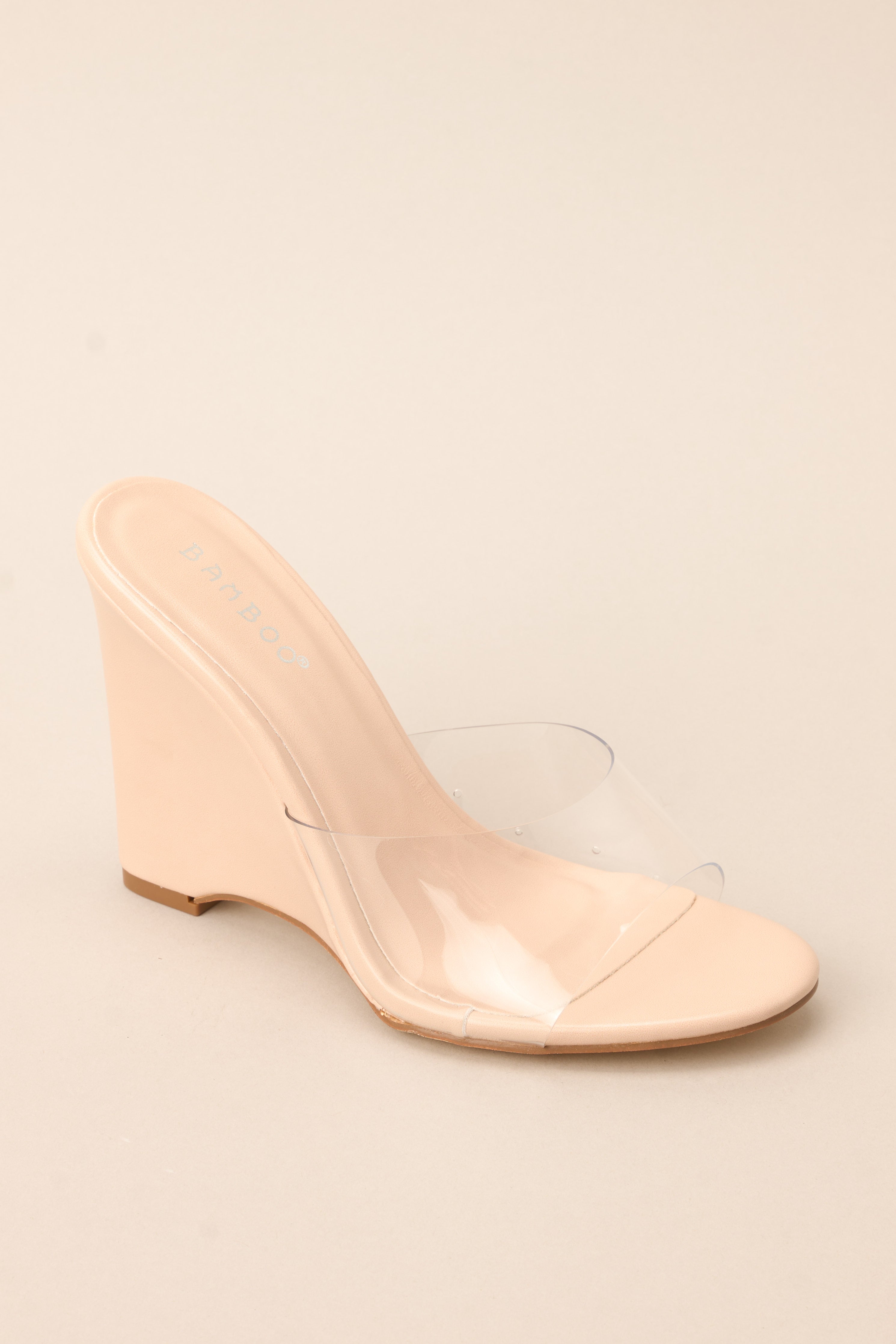 Close up view of these heels that feature a rounded toe, a clear strap over the top of the foot, and a wedged heel.