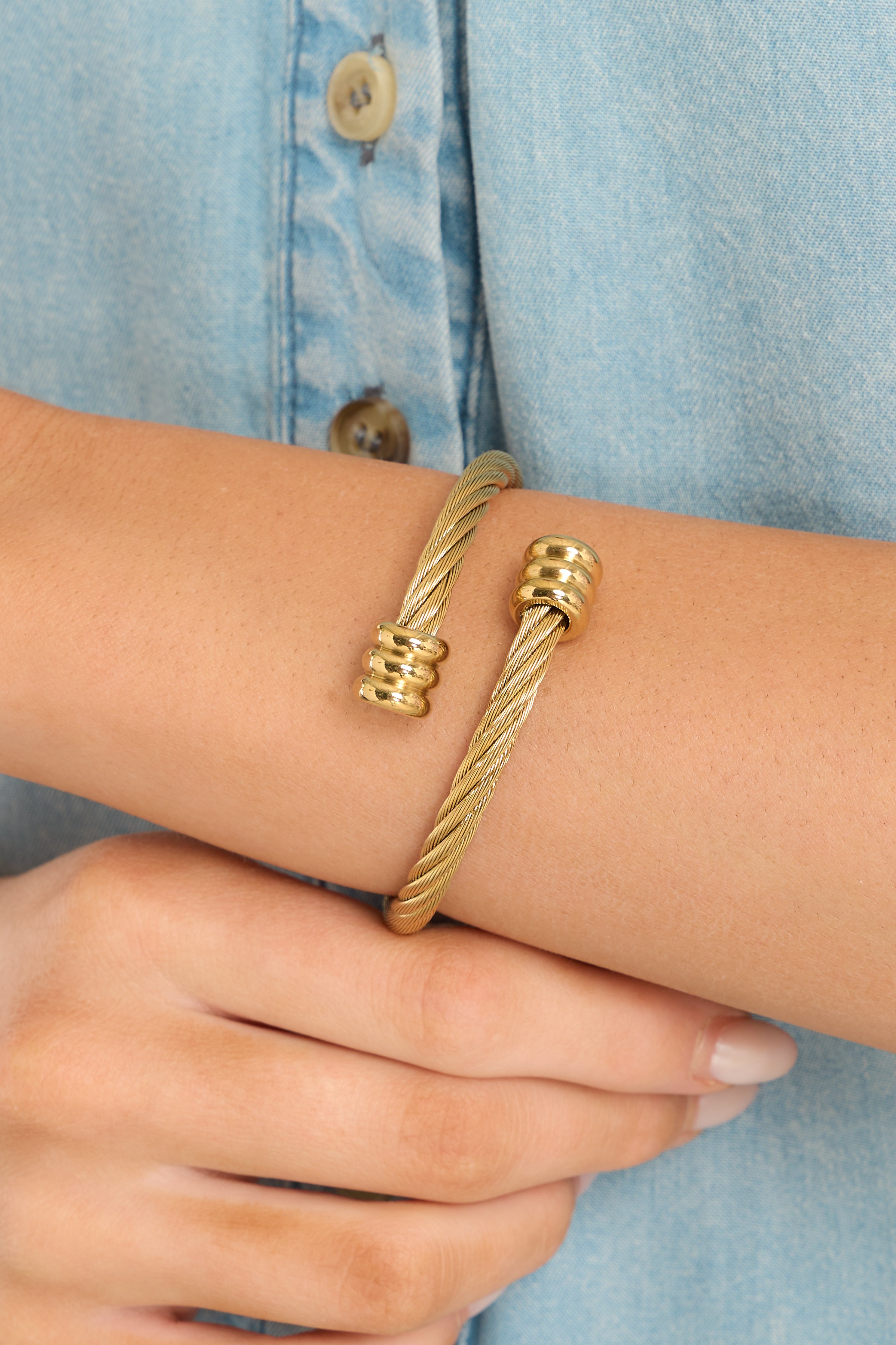 This gold bracelet features gold hardware, a twisted cable design with spiral cuffed ends, and can accommodate most wrist sizes. 