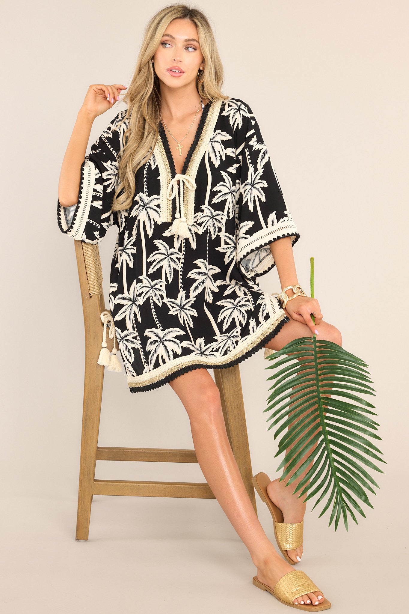 This white and black cover up features a v-neckline with a self-tie feature, crochet detailing, a self-tie belt, a split hemline with self-tie features, and wide sleeves with open knit detailing. 