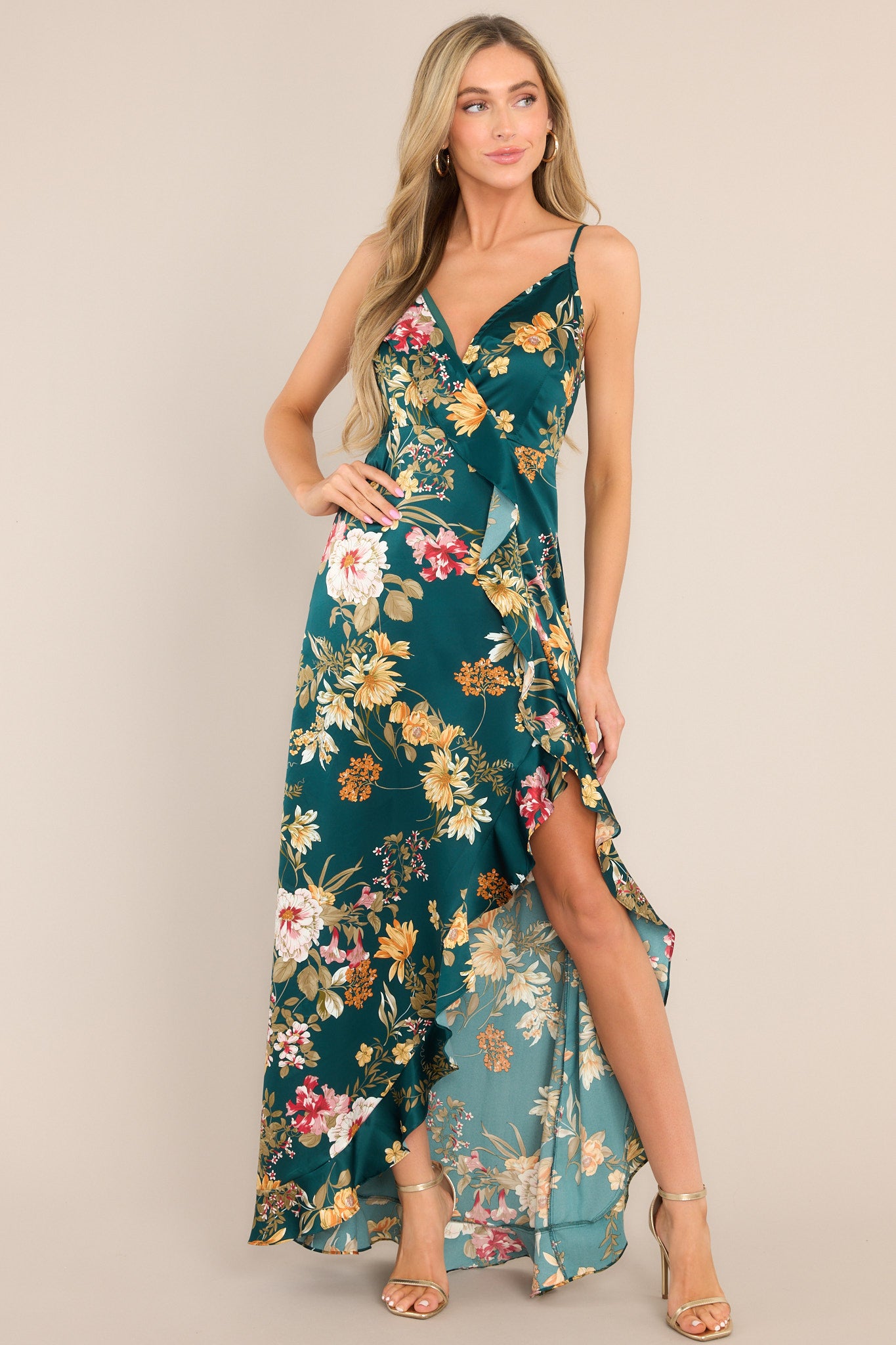 Full body view of this emerald floral dress that features a v-neckline, adjustable straps, an open back, a functional side zipper, a faux wrap design, and a high slit.