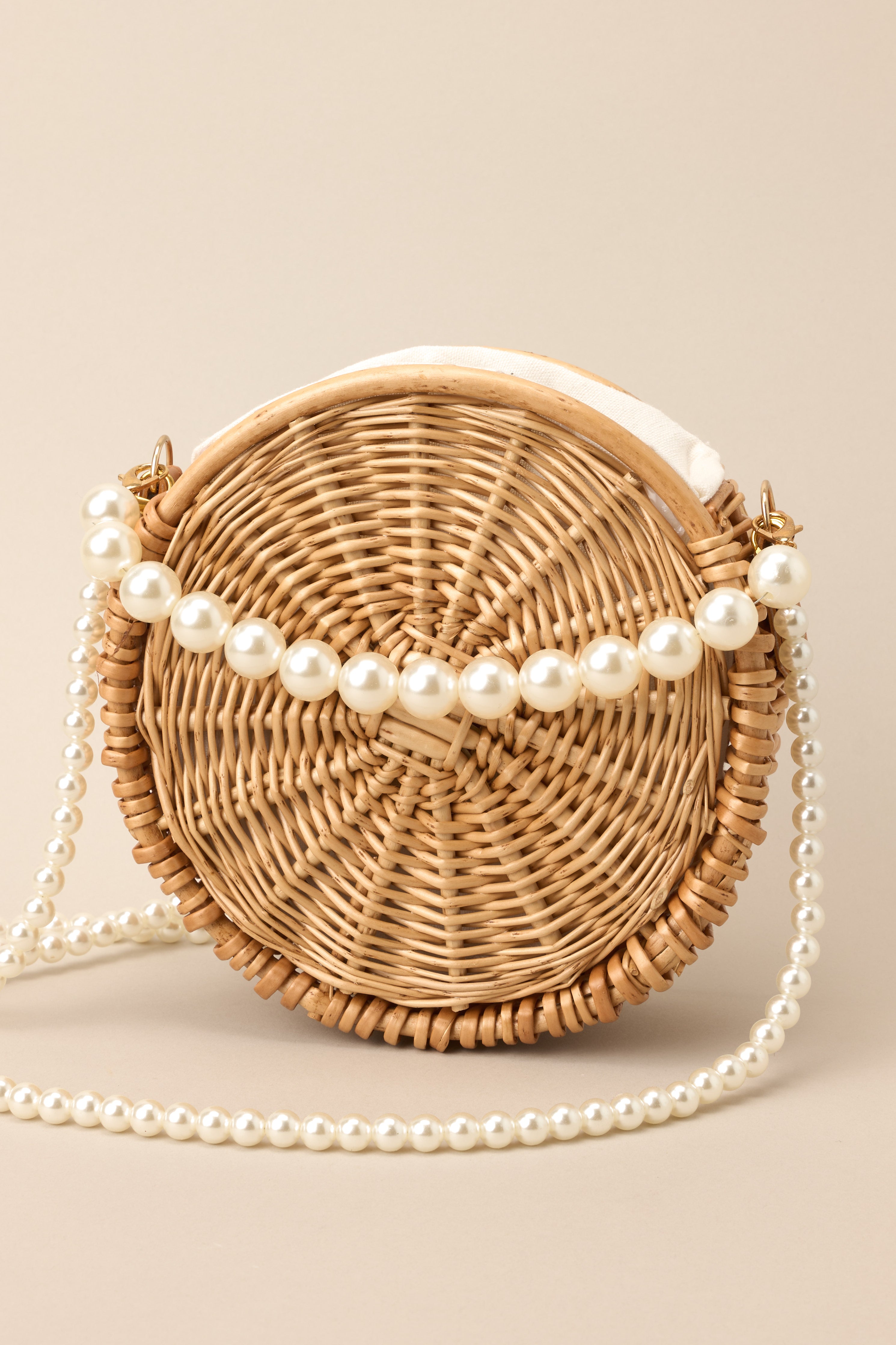 Close up view of this handbag that features gold hardware, 2 removable faux pearl straps, a circular shape, and a drawstring closure.