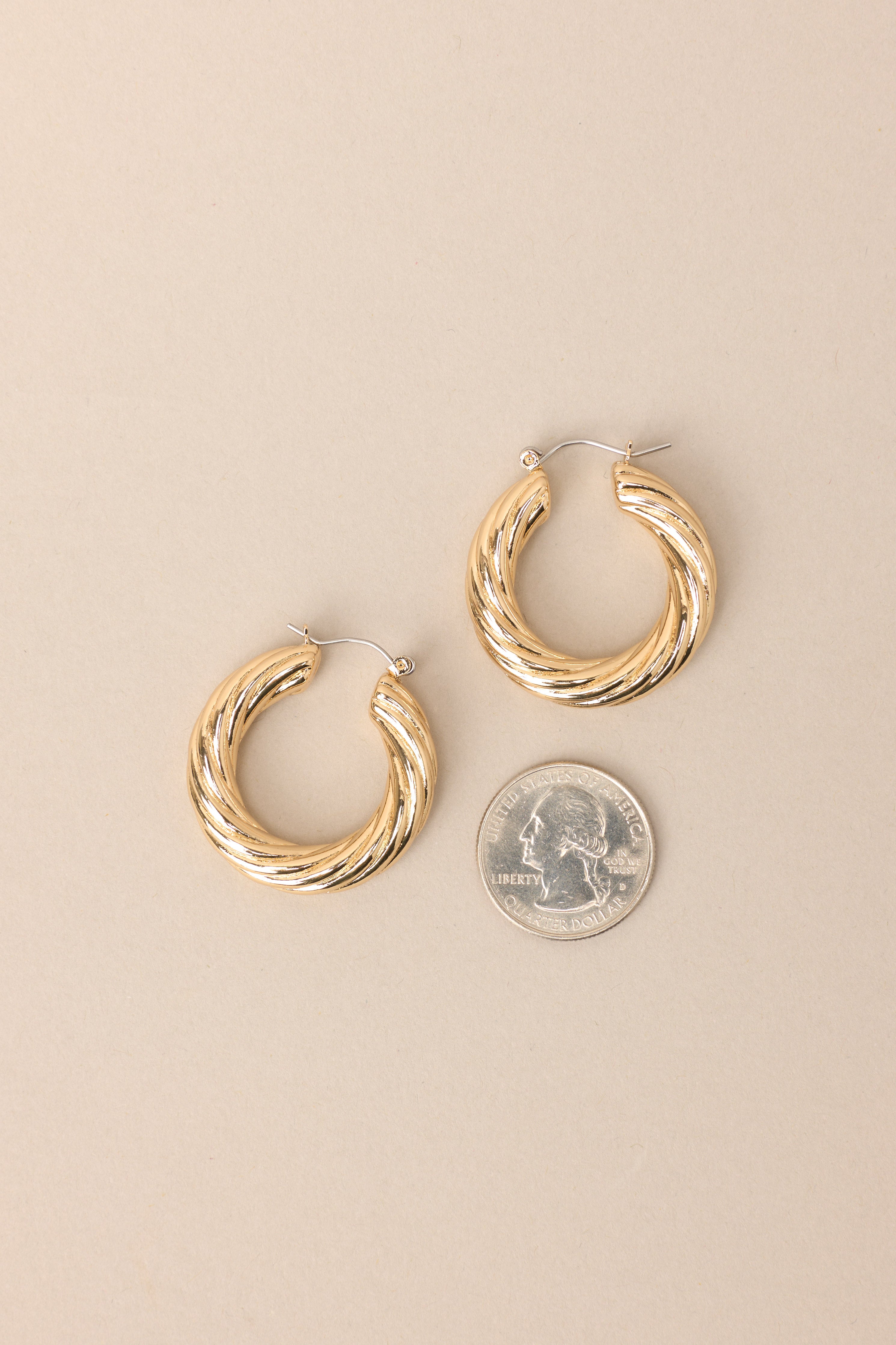 Size comparison of these gold hoops that feature gold hardware, a twisted design, and a lever back closure.