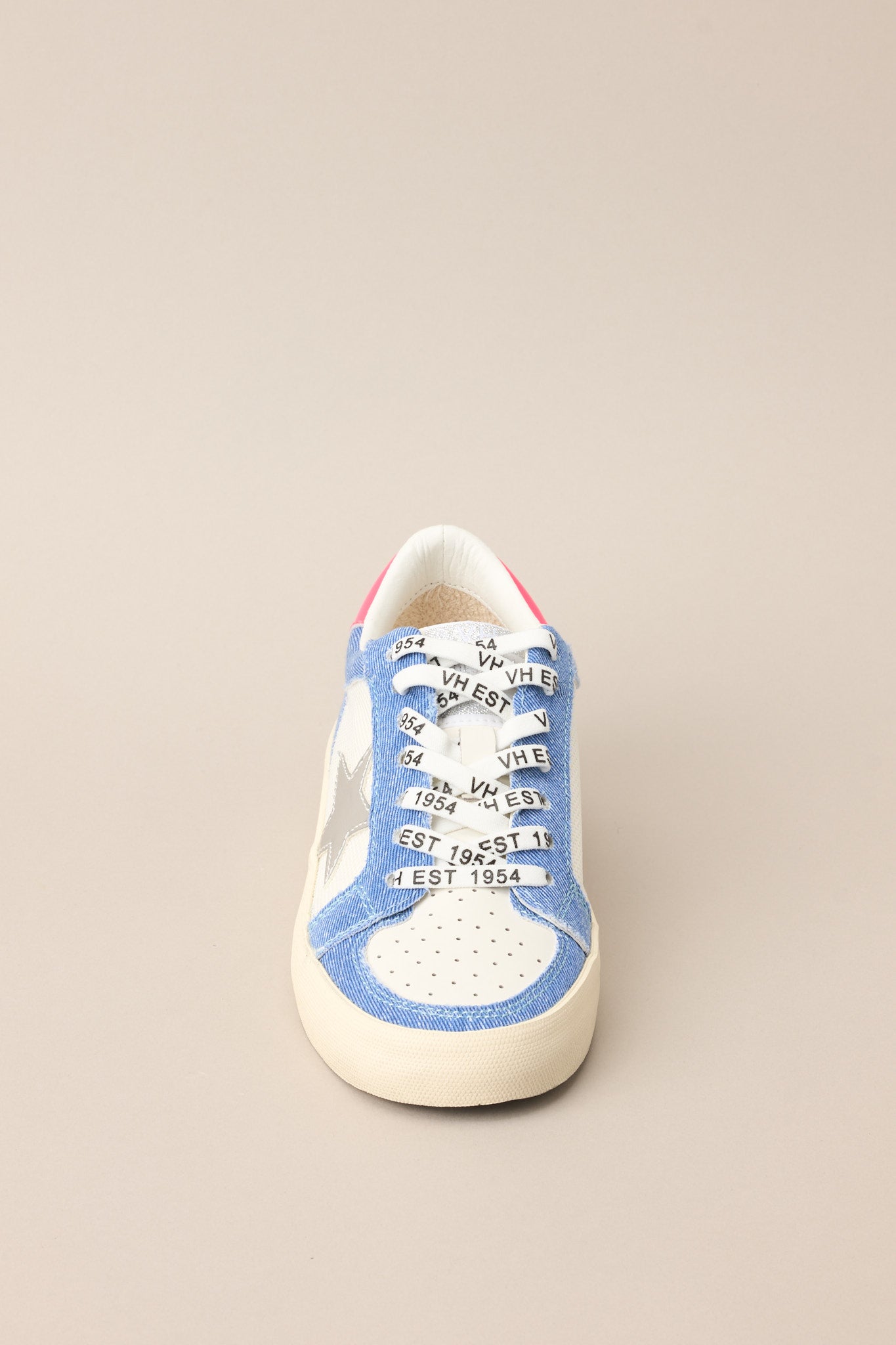 Front view of these sneakers that feature a rounded toe, functional laces, medium wash denim trim, silver stars, and neon pink detailing.