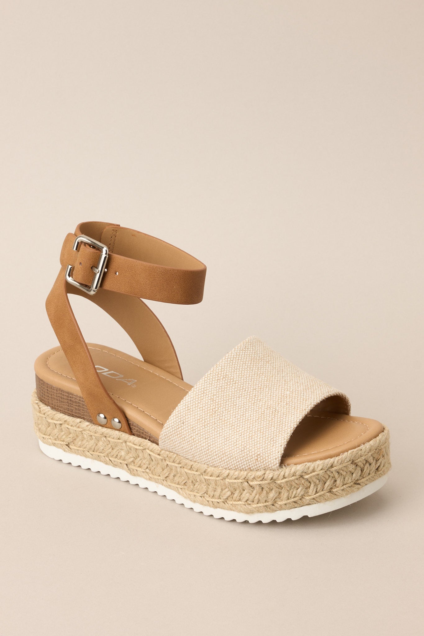 Angled side view of these sandals that feature a rounded toe, silver hardware, a textured strap over the top of the foot, a contrasting strap around the heel and ankle, and a buckle closure.