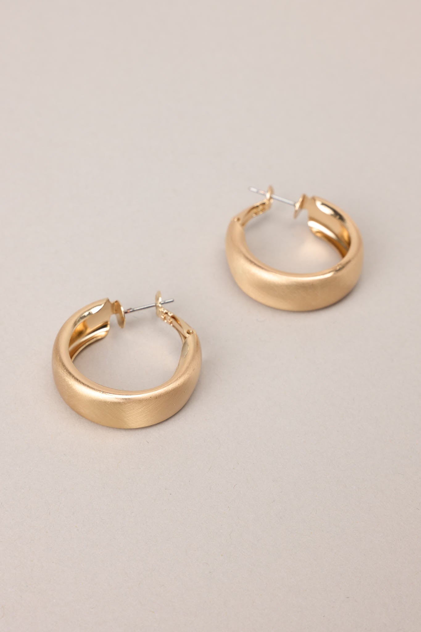 Close up view of these earrings that feature gold hardware, a matte finish, and a functional clasp closure.