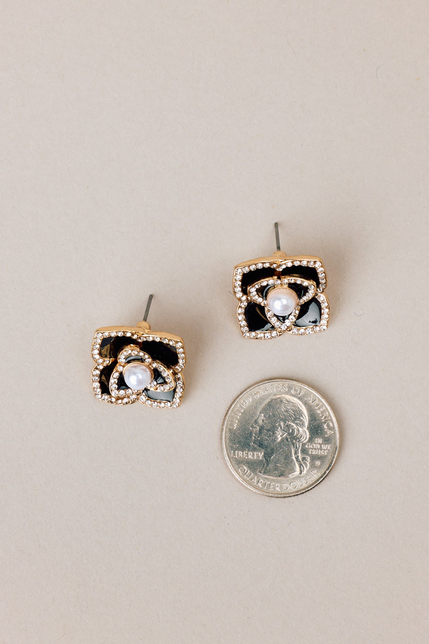 Size comparison of these black pearl earrings that feature gold hardware, a flower design, rhinestone embellishments, a faux pearl detail, and a secure post backing.