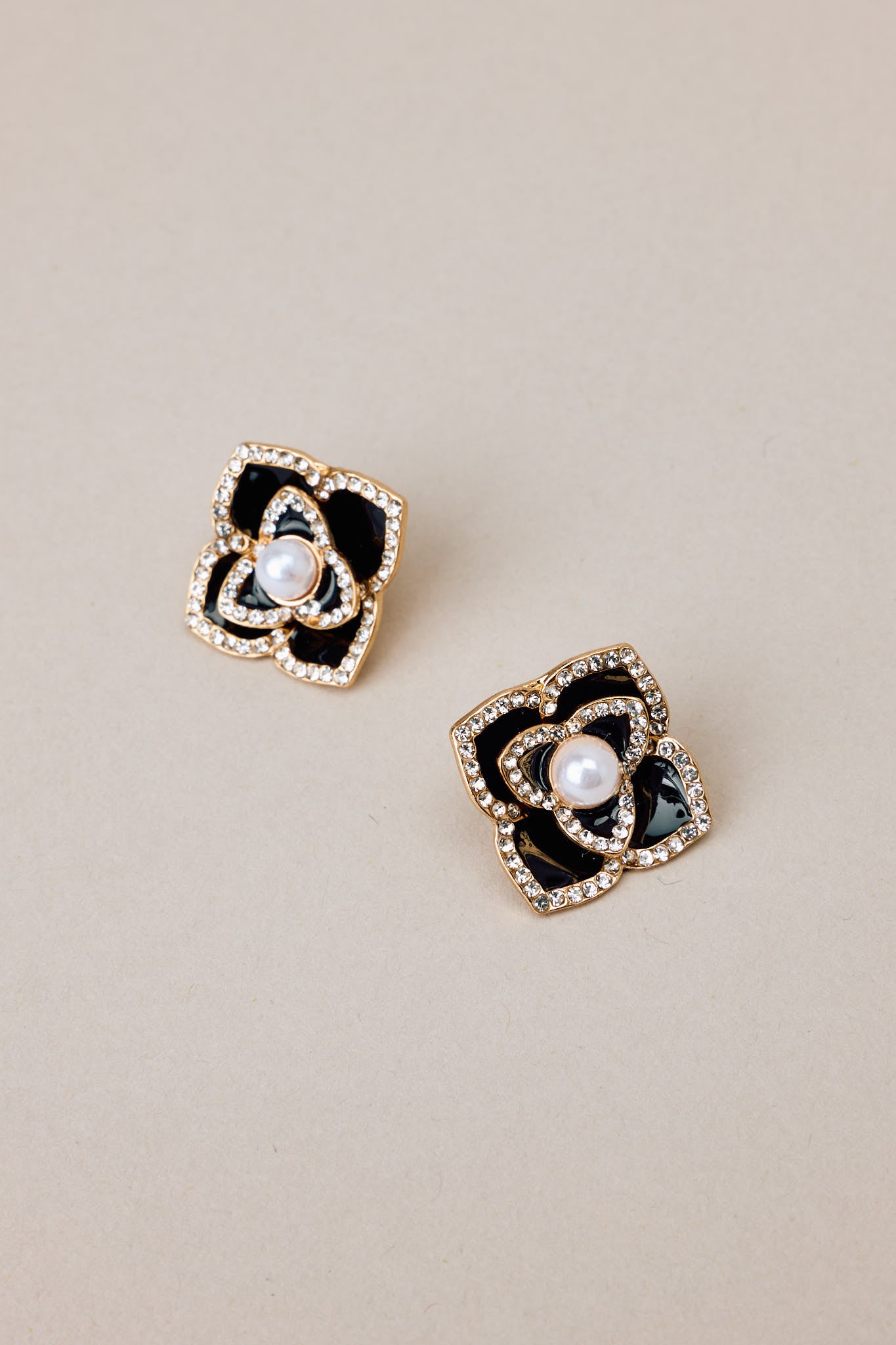 Angled overhead view of these black pearl earrings that feature gold hardware, a flower design, rhinestone embellishments, a faux pearl detail, and a secure post backing.