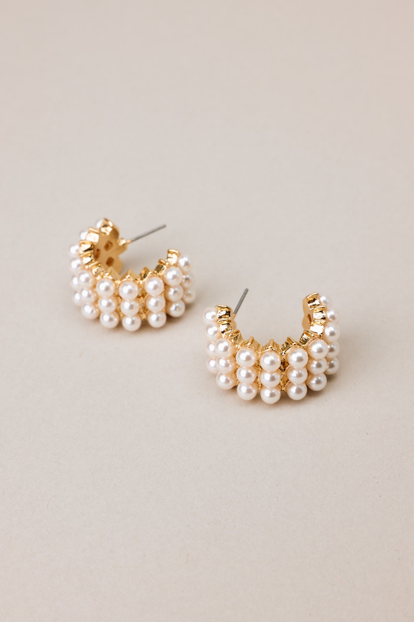 Close up view of these earrings that feature gold hardware, rows of faux pearls, an open circle design, and secure post backings.