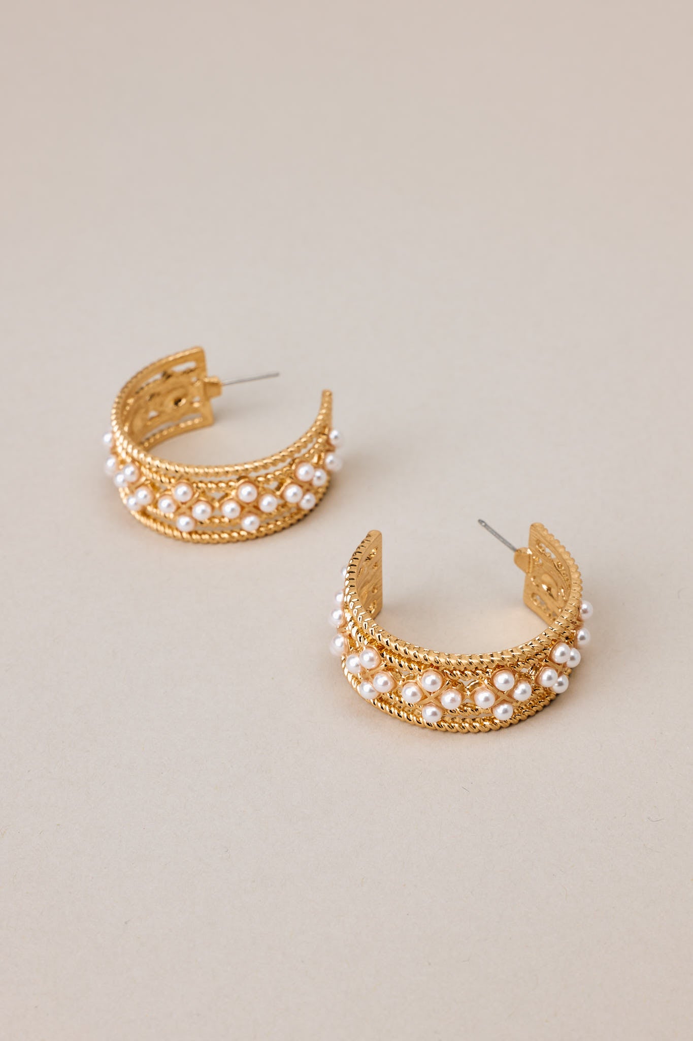 Angled overhead view of these hoops that feature gold hardware, faux pearl embellishments, and secure post backings.