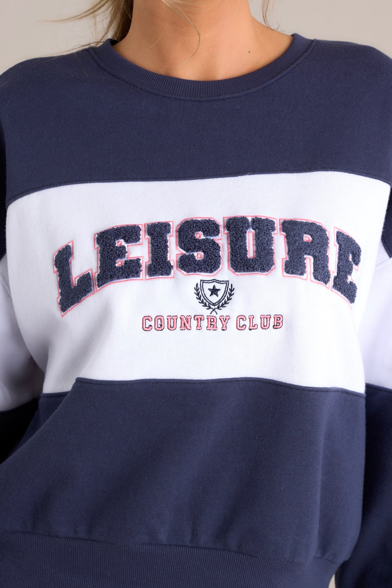 Close up view of this sweatshirt that features a ribbed crew neckline, high contrast color blocking, embroidered & terry cloth wording, ribbed cuffed sleeves, and a ribbed hemline.